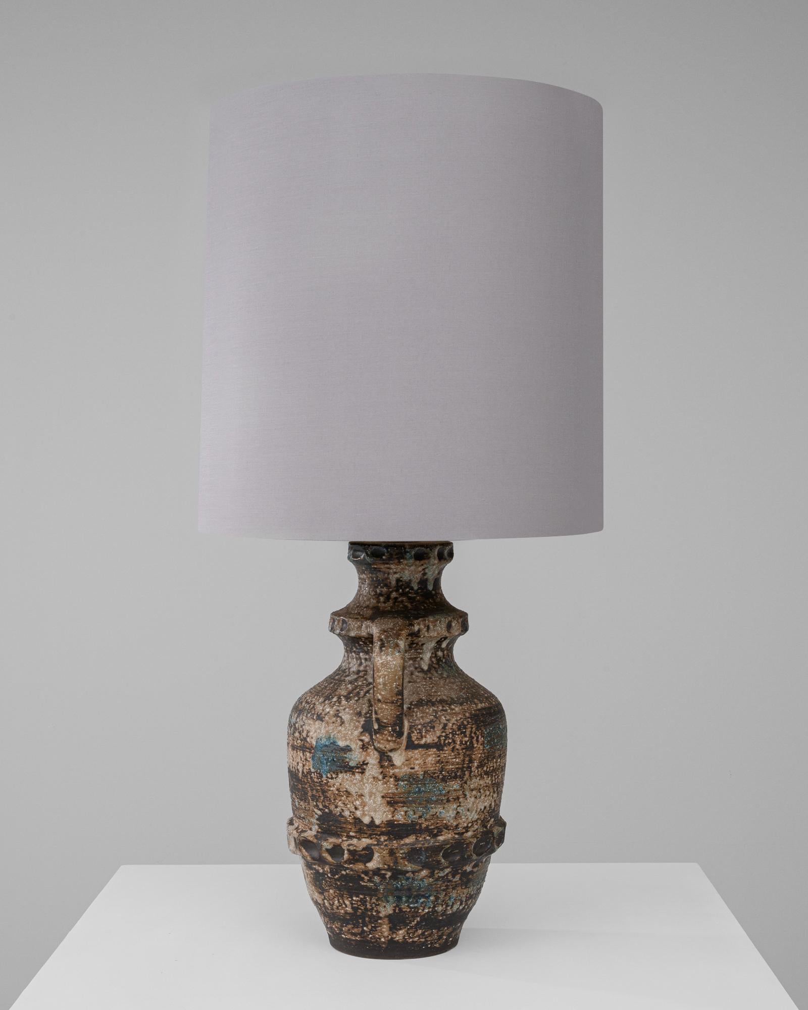 Infuse your living space with the rich texture and storied beauty of the 20th Century German Ceramic Table Lamp. The lamp's base is a masterpiece of ceramic artistry, with a body that evokes the ancient world through its amphora-like shape and