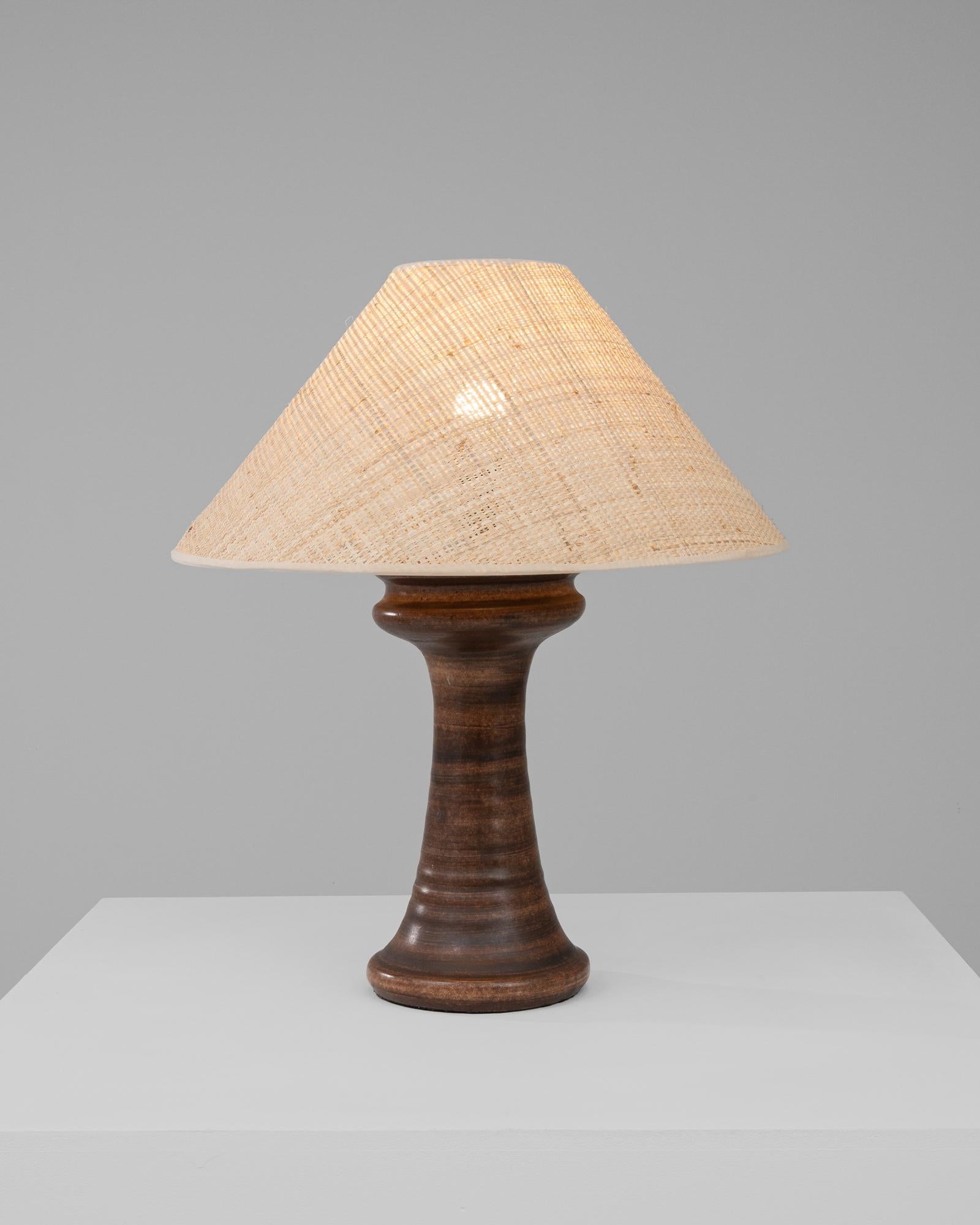 Discover a fusion of natural textures with this 20th Century German Ceramic Table Lamp, a piece that seamlessly blends the organic with the functional. The base of the lamp is a robust column of dark, earthen-toned ceramic, its surface swirling with