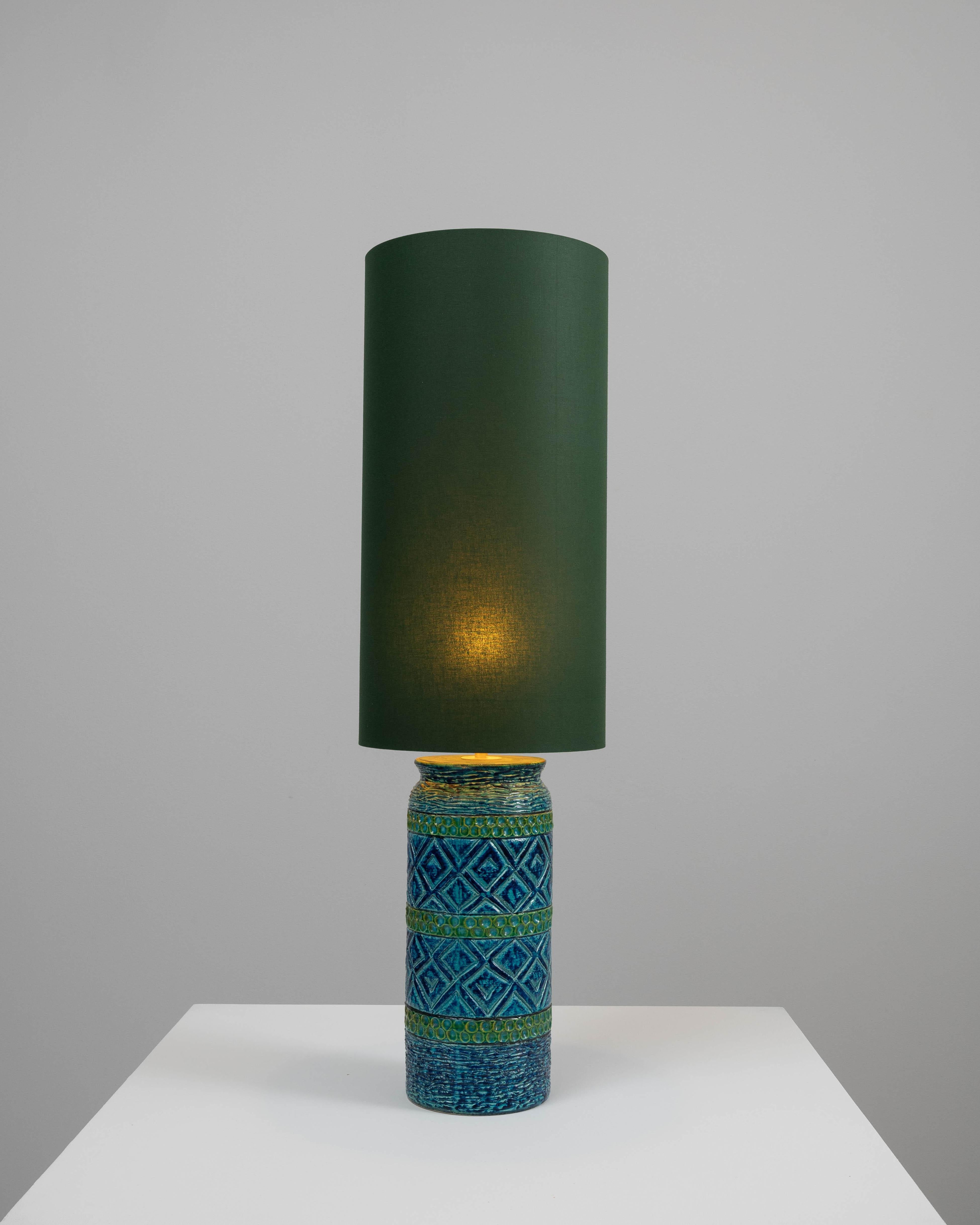 Step into a world of vibrant color and artistry with this 20th-century German ceramic table lamp. The lamp's base dazzles with its intricate patterns and lush blues and greens, evoking the rich complexity of a mosaic. The handmade ceramic work