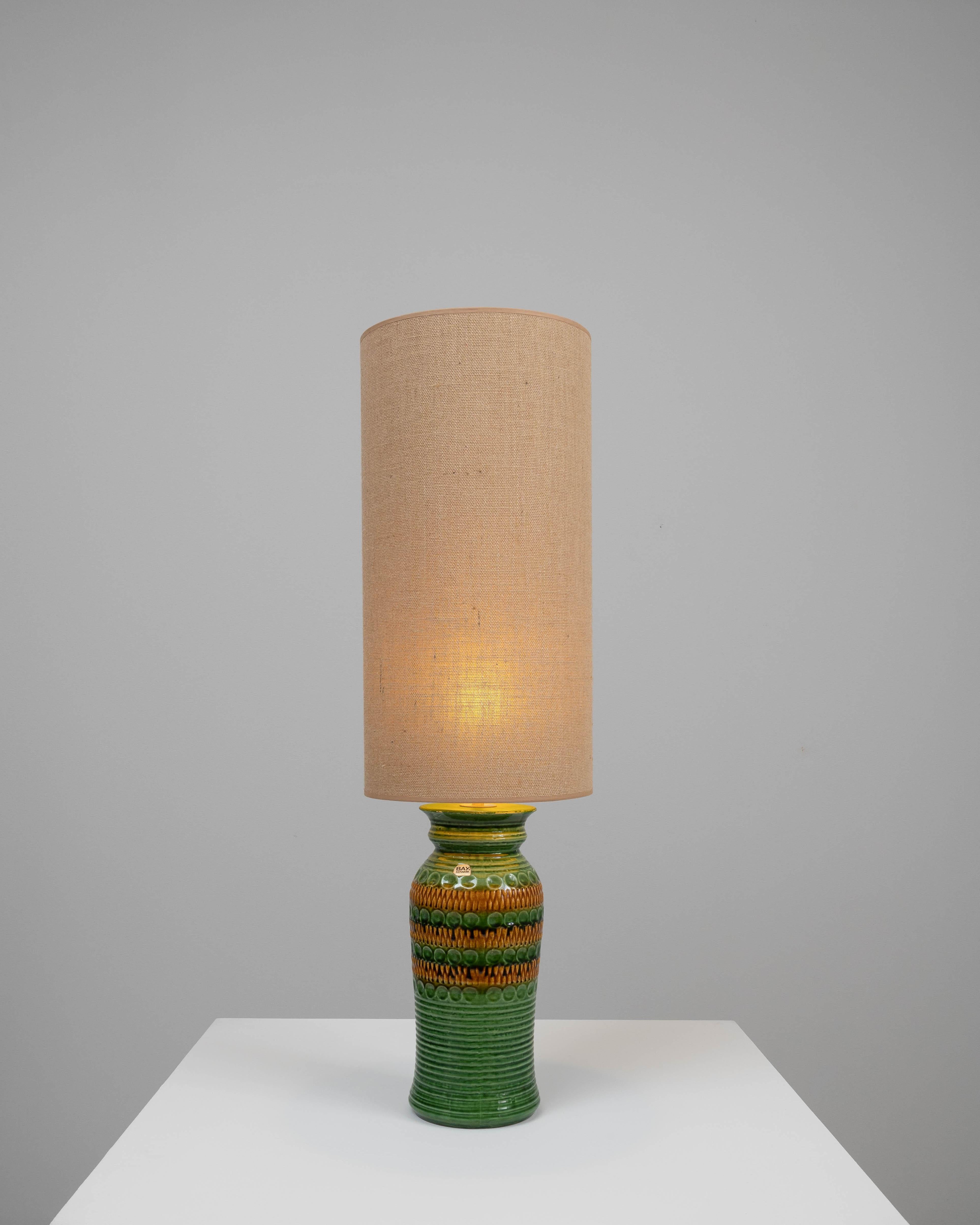 This charming 20th-century German ceramic table lamp combines the organic appeal of pottery with functional design. The lamp's base is a masterpiece of ceramic art, featuring vibrant green hues and intriguing textures that mimic natural forms. The