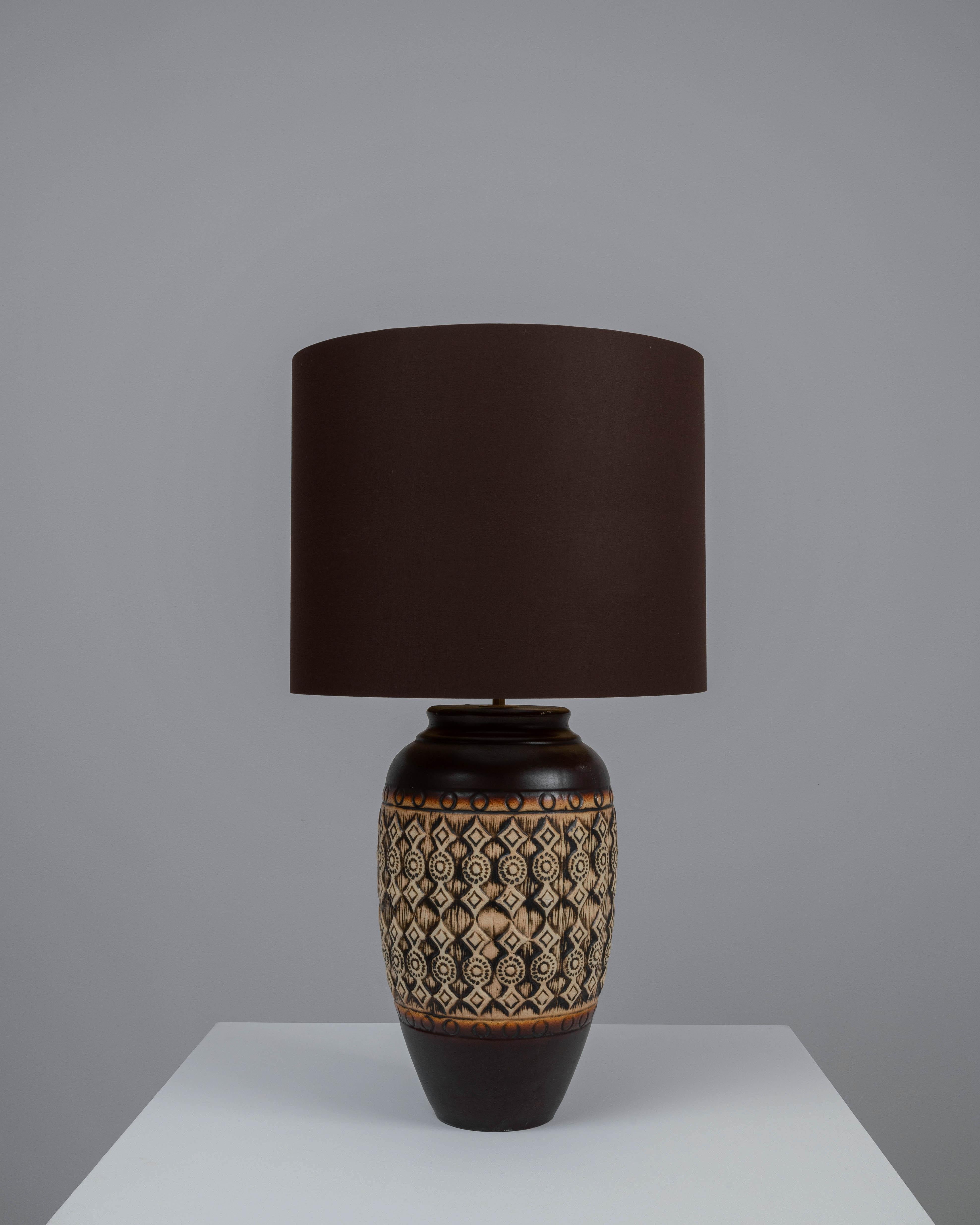 Cette lampe de table en céramique allemande du XXe siècle est une célébration des motifs et des textures. La base de la lampe est ornée d'un motif complexe d'inspiration tribale, gravé dans la céramique et animé d'une glaçure chaude et terreuse qui