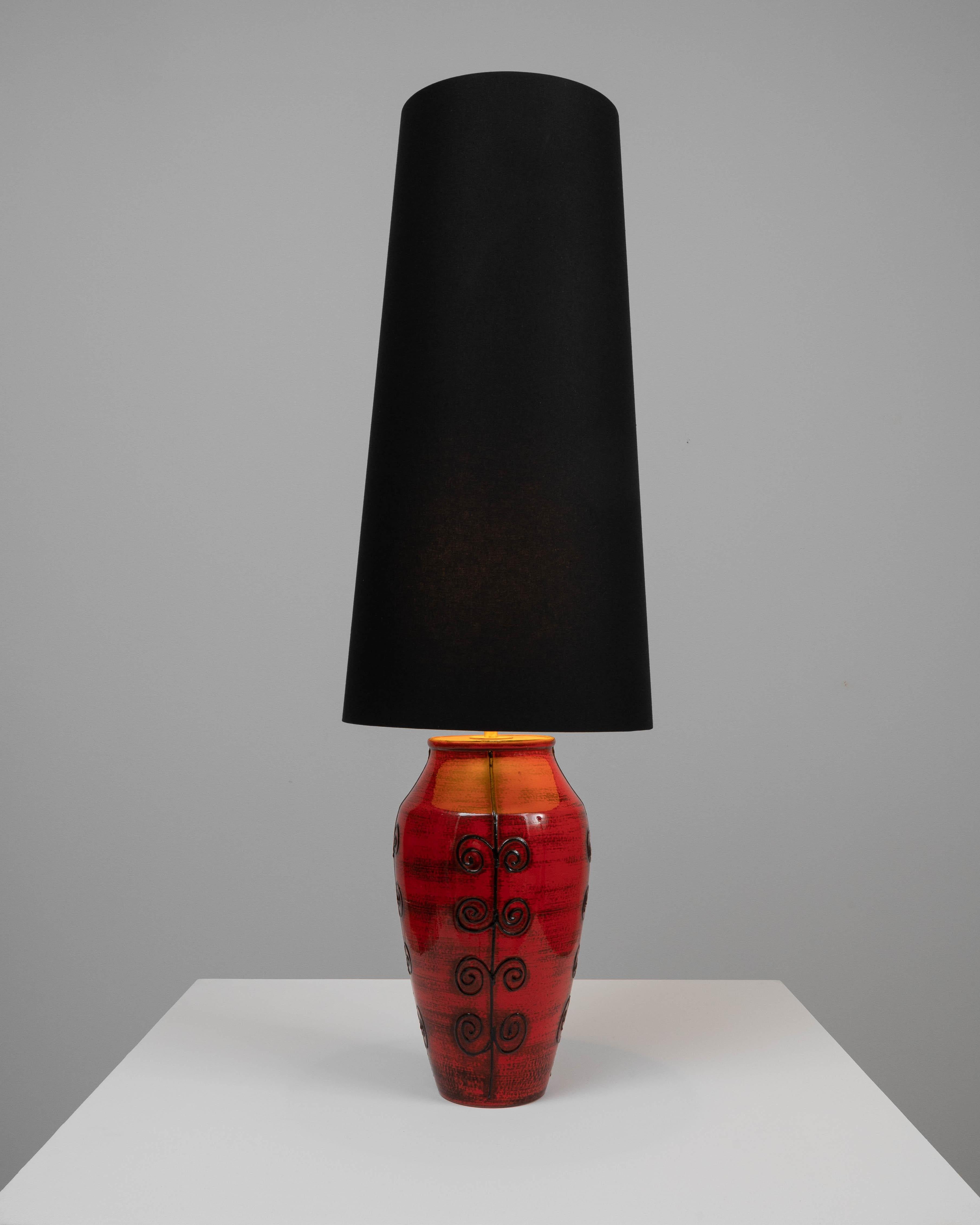 This eye-catching 20th-century German ceramic table lamp is a vibrant statement piece. The bold red base, with its glossy finish and swirling black accents, offers a dramatic contrast to the sleek black lampshade. The lamp's design combines the