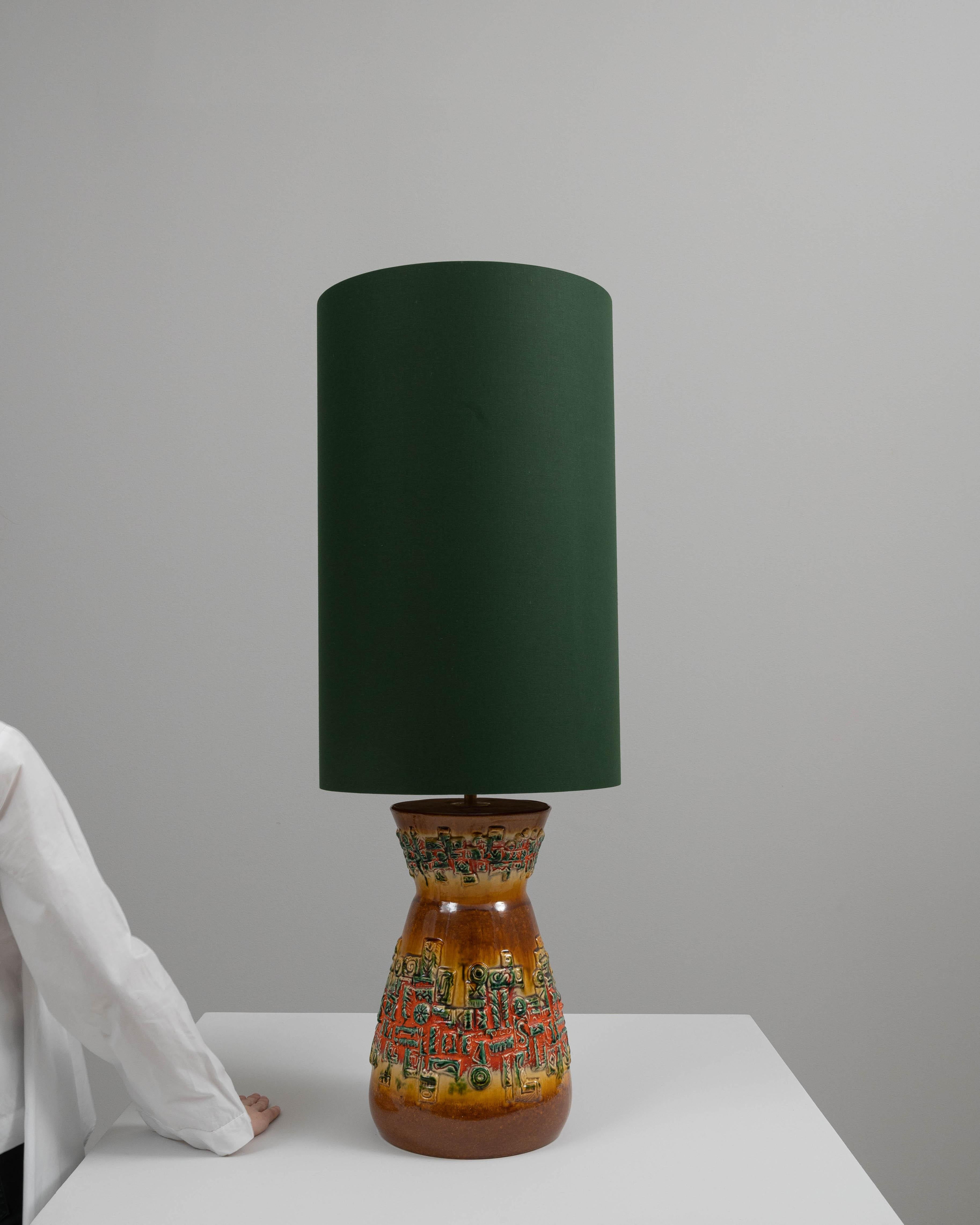 This captivating 20th-century German ceramic table lamp is an artful blend of functionality and detailed craftsmanship. The base is adorned with a complex, raised pattern featuring hints of earthy tones and vibrant greens, giving it a textured,
