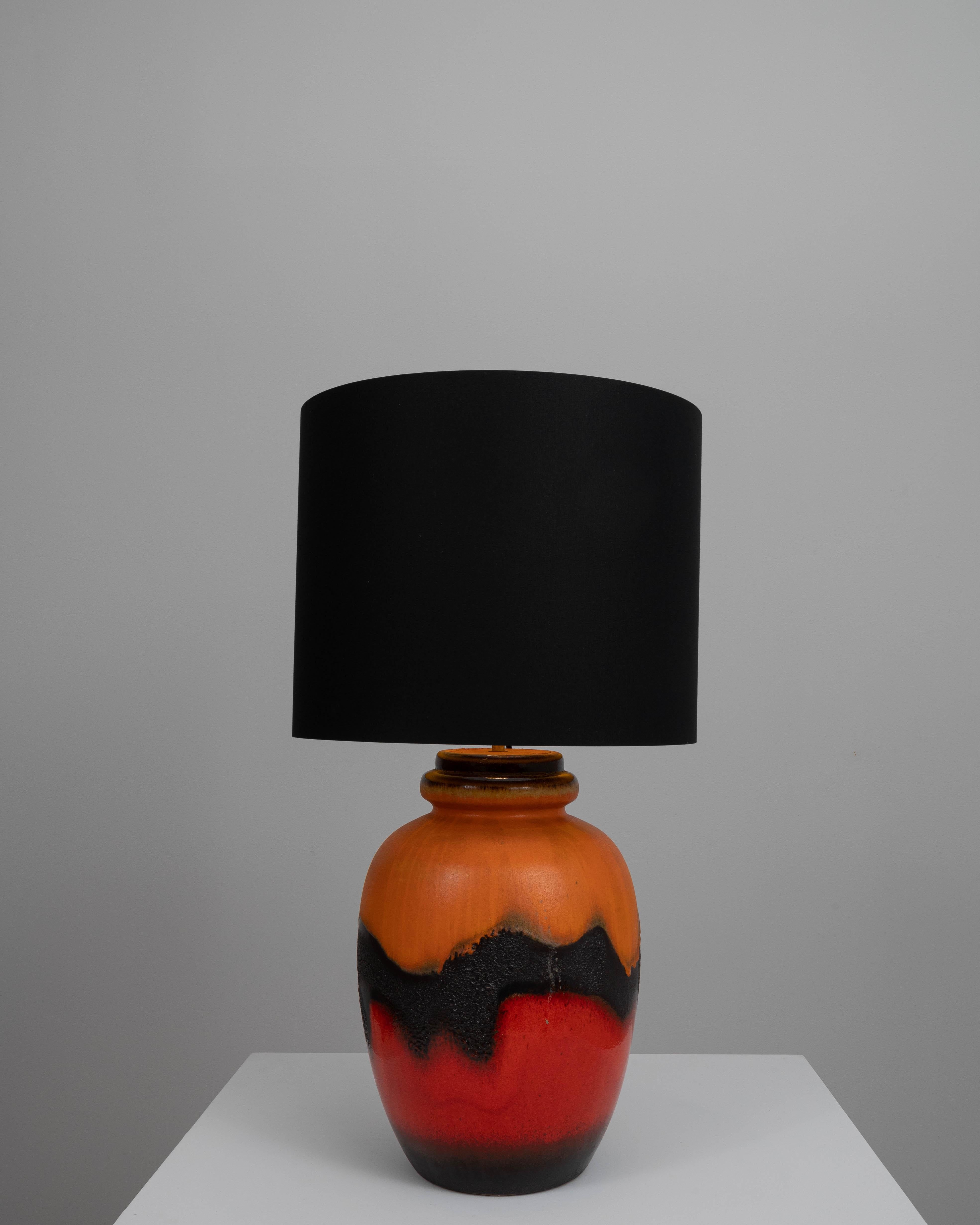 Add a bold statement to your interior with this striking 20th-century German ceramic table lamp. The vivid, fiery red base is artfully contrasted with a deep black texture, resembling the volcanic lava flows, and topped with a sleek black shade.