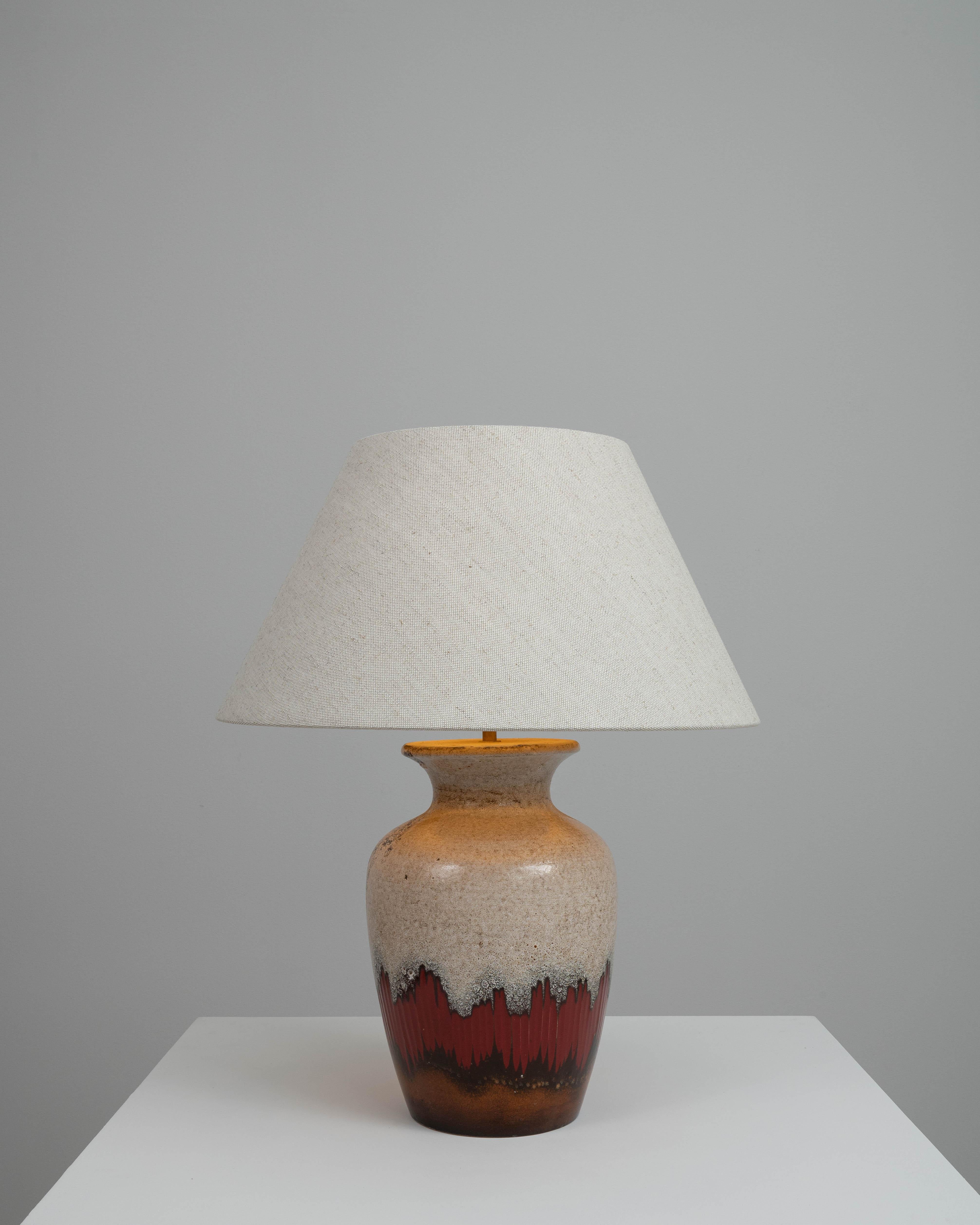 Cette lampe de table en céramique allemande du XXe siècle est une splendide fusion de l'art et de la fonction. Cette pièce promet d'être bien plus qu'une simple source de lumière dans votre espace de vie. La forme robuste de la lampe est ornée d'une