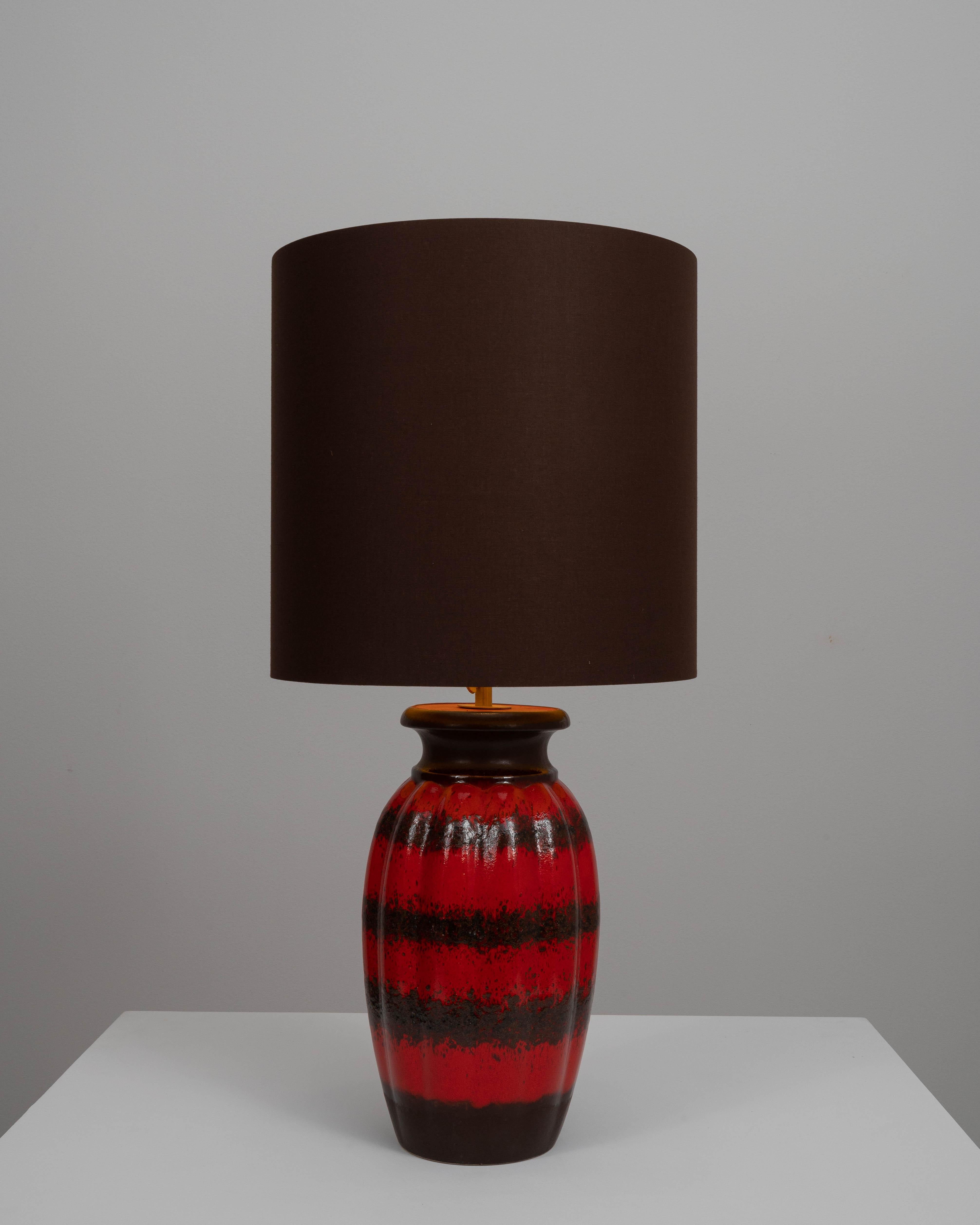 This 20th Century German Ceramic Table Lamp exemplifies the bold and expressive design sensibilities that characterized the era. The lamp's base is a vessel of vibrant artistry, with a rich, crimson glaze that drips over a glossy black ceramic
