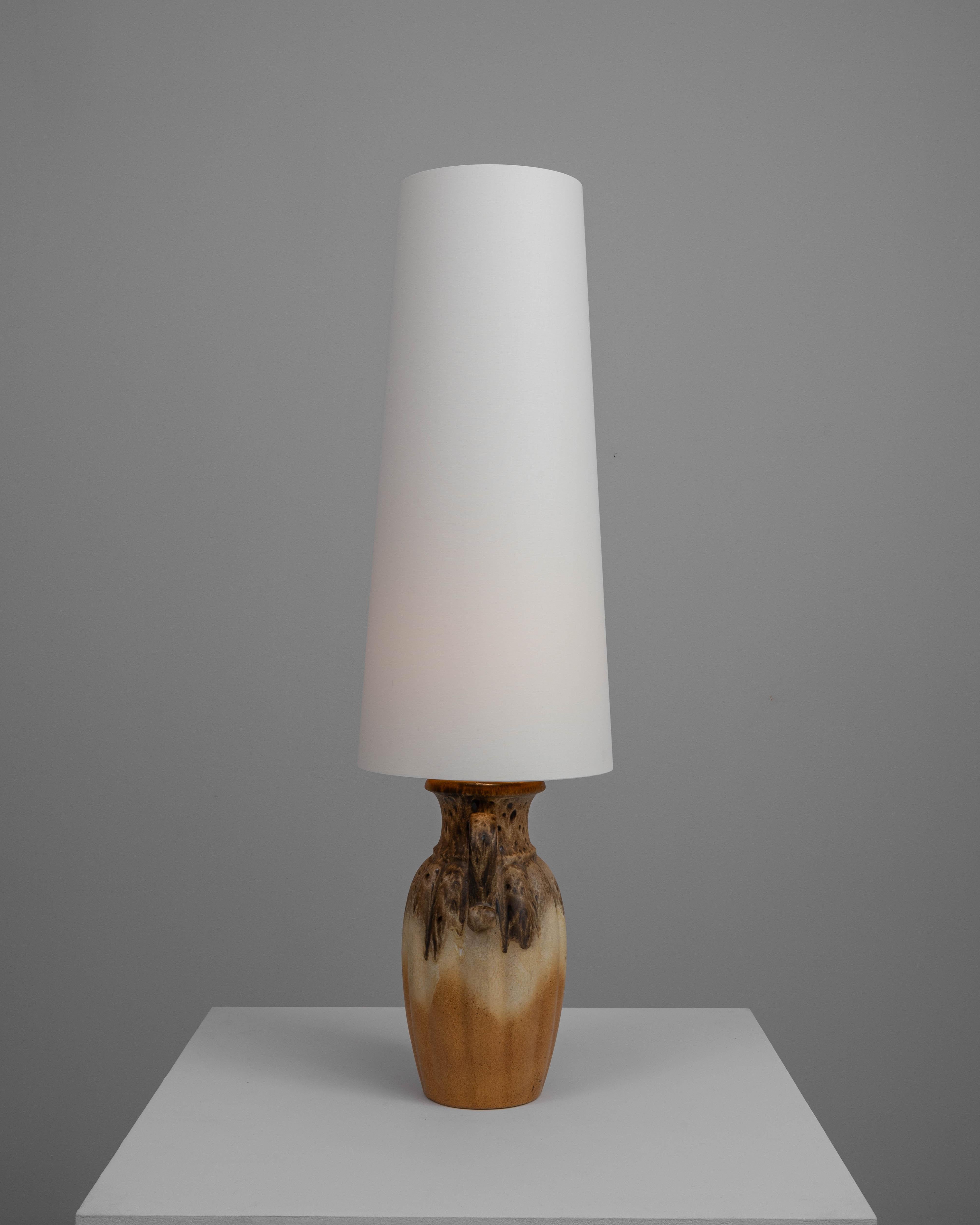 Cette lampe de table en céramique allemande du XXe siècle est une pièce exemplaire de l'artisanat du milieu du siècle. La base présente une forme robuste et naturelle avec une glaçure dynamique et fluide qui combine des tons de brun terreux avec des