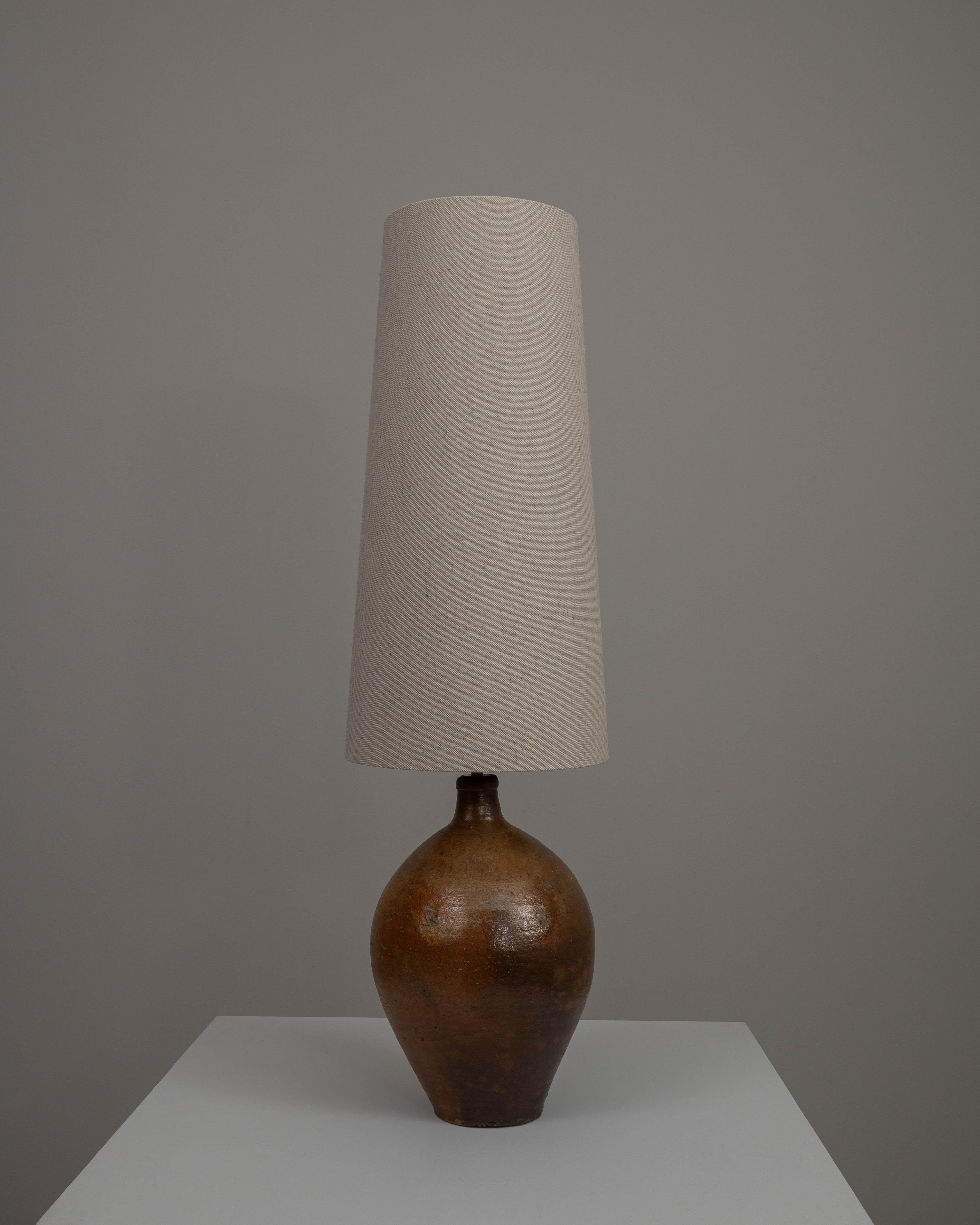 Cette lampe de table en céramique allemande du XXe siècle allie l'attrait de la poterie traditionnelle à la simplicité du design moderne. La base en céramique robuste rappelle la faïence ancienne, avec une glaçure brune robuste et chaude qui