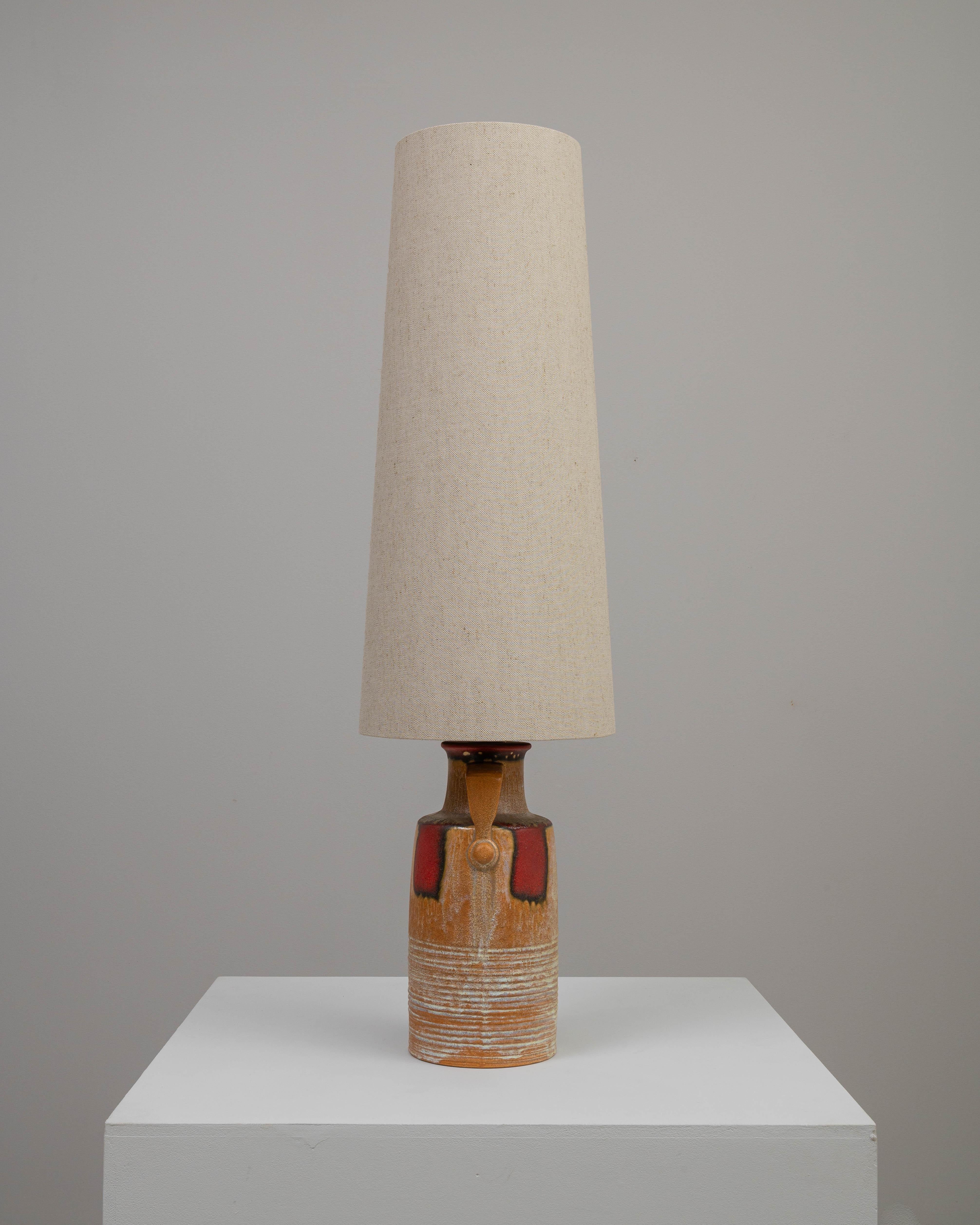 Cette lampe à poser en céramique allemande du XXe siècle est un mélange distinctif d'esthétique rustique et de design du milieu du siècle. La base robuste, en forme de cruche, a un attrait terreux avec ses stries horizontales texturées et une