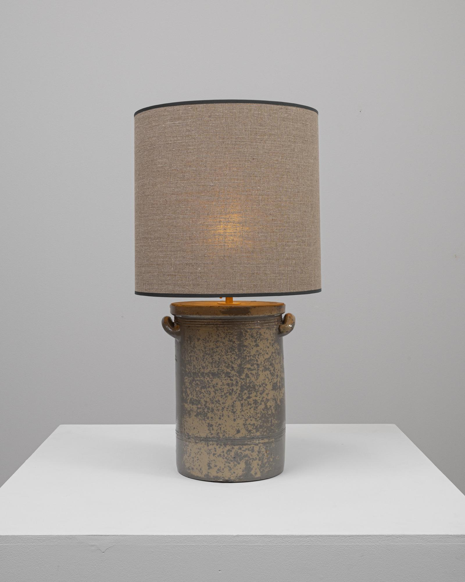 This 20th Century German Ceramic Table Lamp embodies the rugged, unrefined beauty of industrial design. The base, reminiscent of a milk pail, boasts a utilitarian form with an intriguing speckled finish that adds texture and visual interest. Its