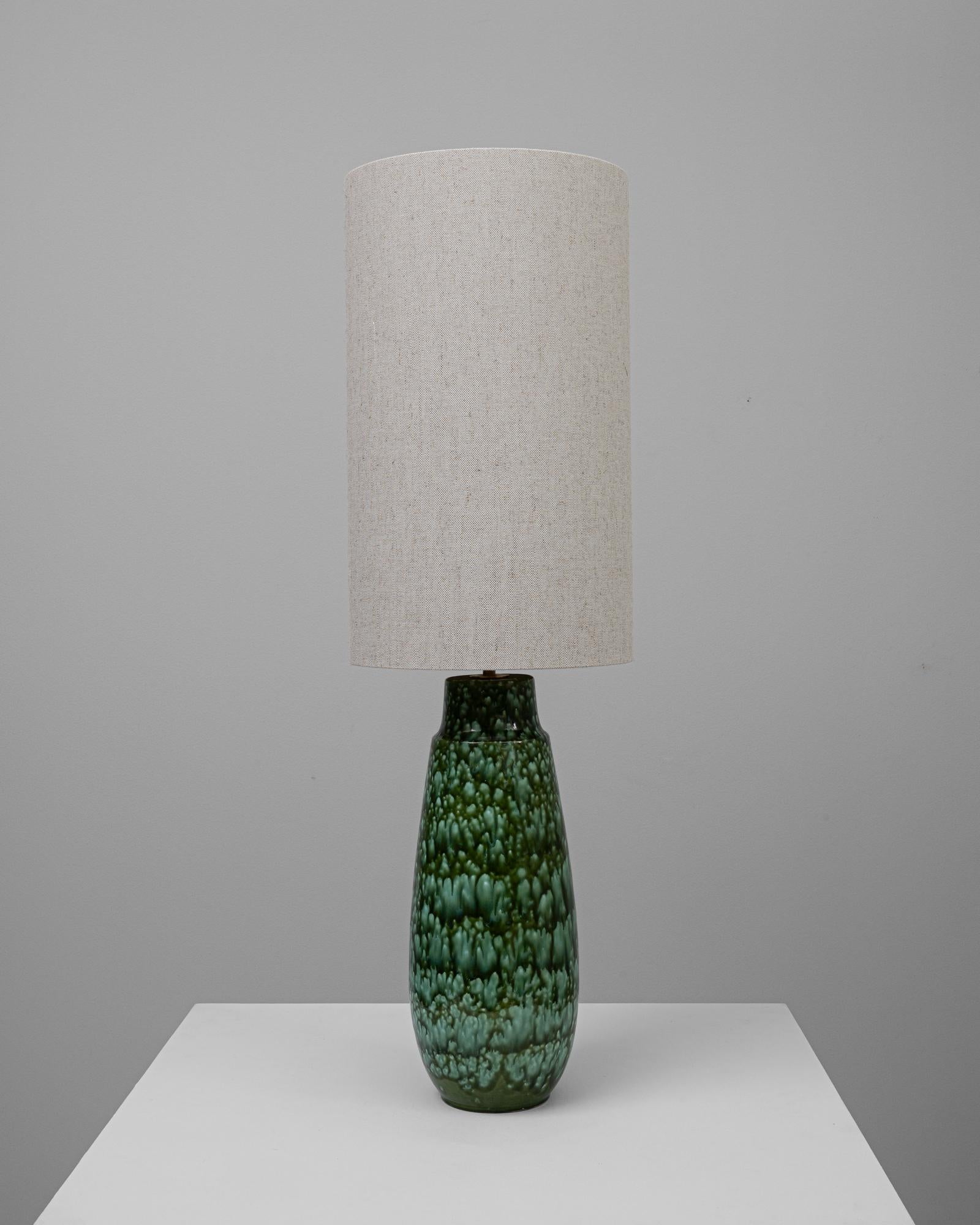 Cette lampe de table en céramique allemande du XXe siècle présente une base qui s'inspire des textures luxuriantes du monde naturel. Sa glaçure d'un vert éclatant, avec un motif en relief unique, rappelle les écailles d'une pomme de pin ou le