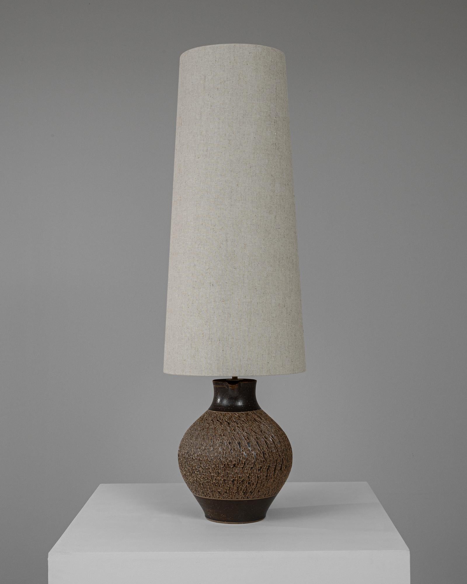 This charming 20th Century German ceramic table lamp offers a blend of rustic allure and functional design, making it a delightful addition to any room. The lamp's base is crafted from ceramic with a rough, textured finish and a deep brown hue that
