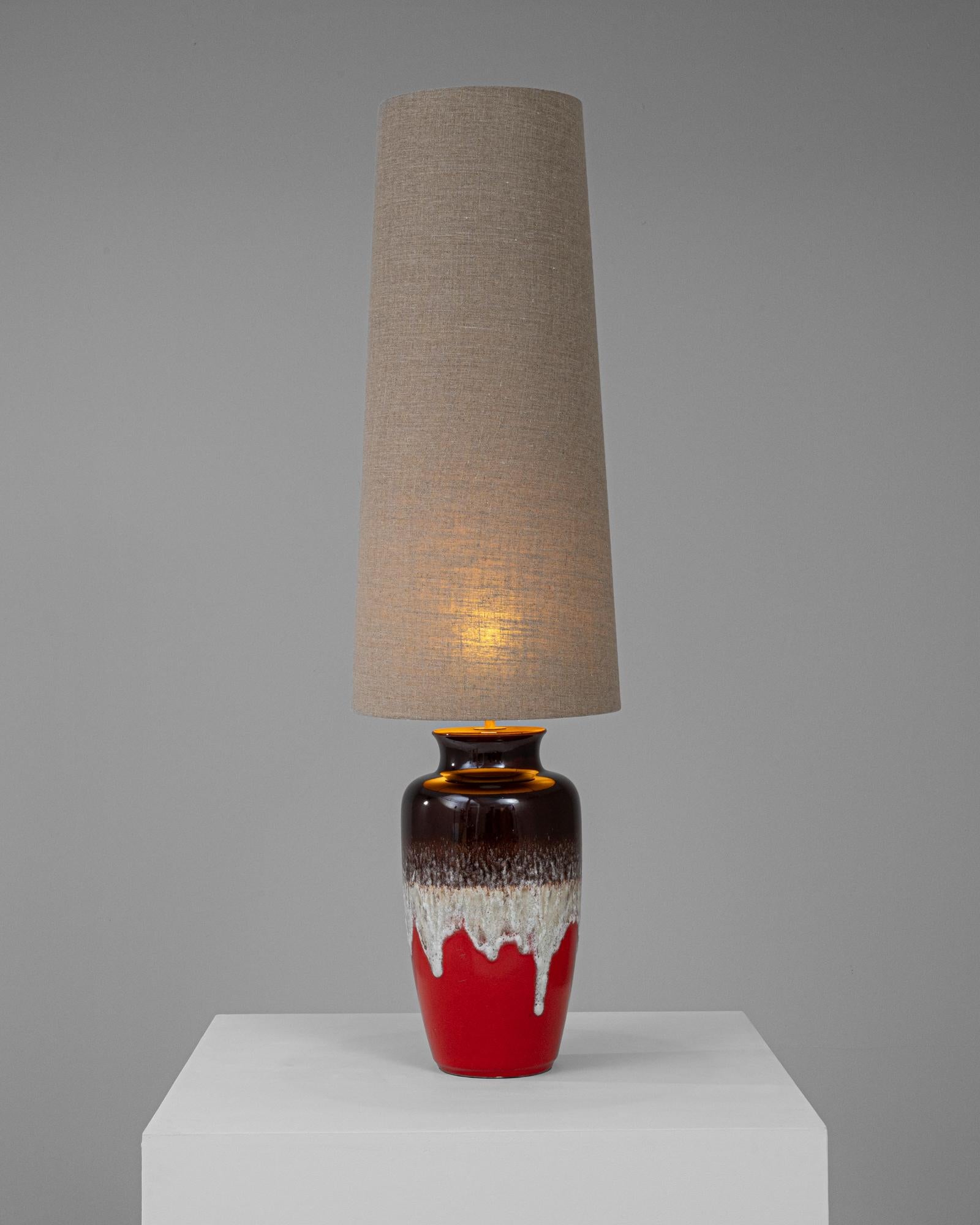 This striking 20th Century German ceramic table lamp brings a bold and artistic flair to any interior. The lamp's base is a masterpiece of ceramic design, featuring a vibrant red color with a dramatic, dripping white and brown glaze that adds an