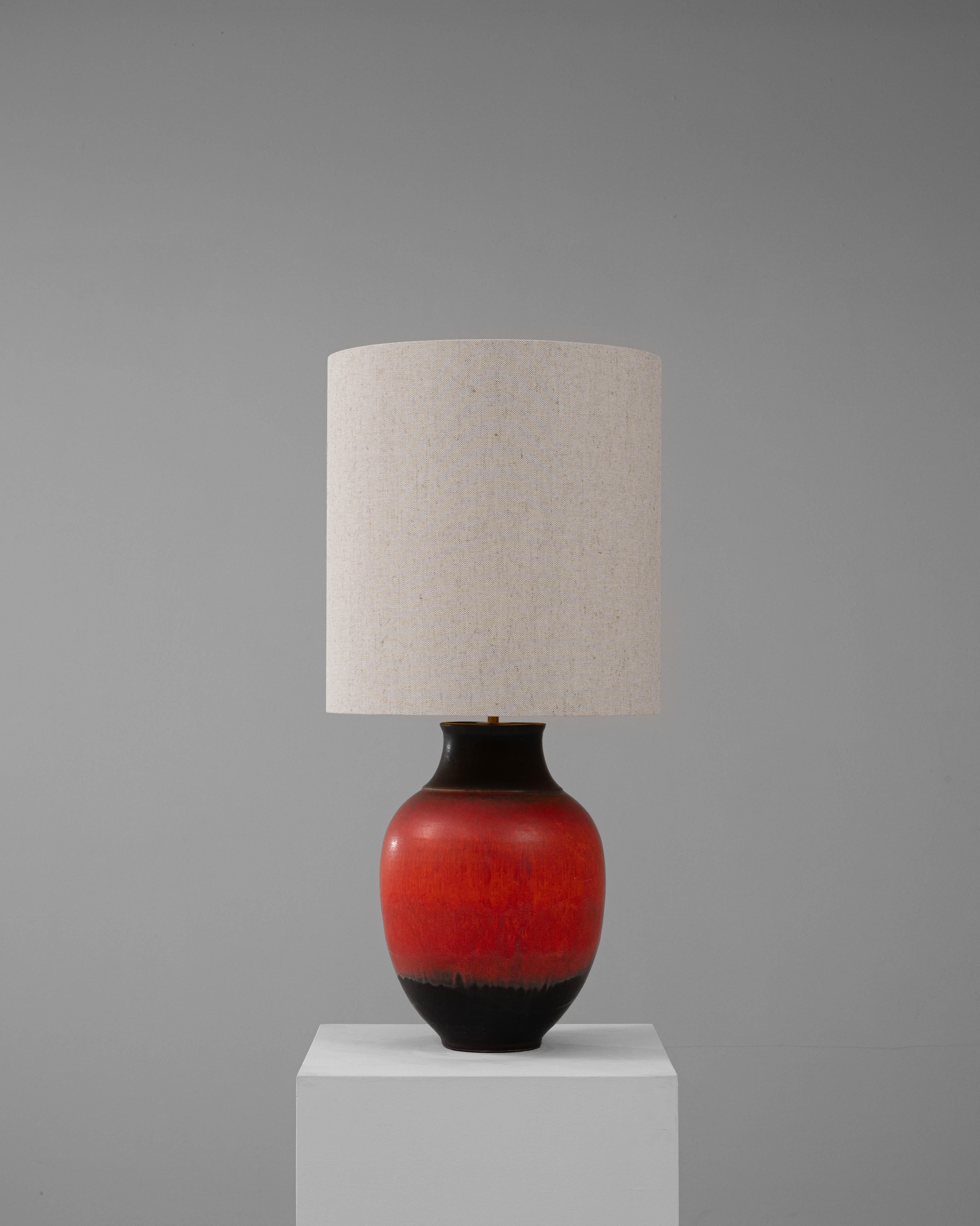 Cette lampe de table en céramique allemande du XXe siècle se distingue par sa glaçure audacieuse et vibrante qui passe sans transition du rouge profond au noir, ajoutant une touche dramatique à n'importe quel espace. La base en céramique en forme de