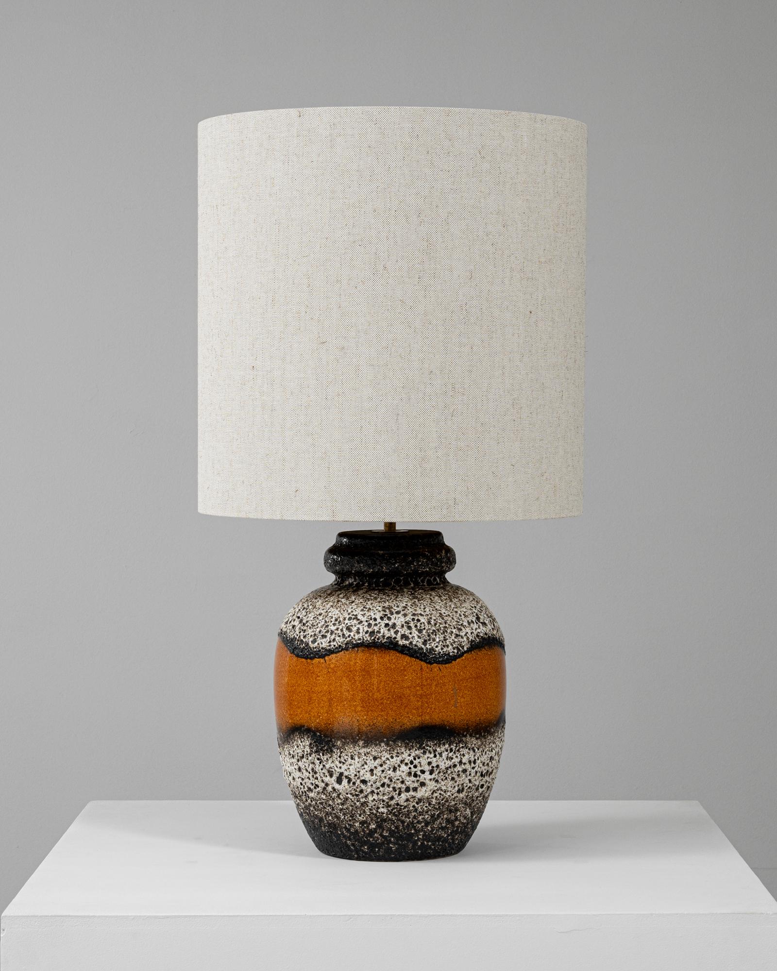 Cette lampe de table en céramique allemande du XXe siècle respire la sophistication moderne du milieu du siècle grâce à son design texturé unique. La lampe présente une glaçure de lave orange et noire saisissante, se fondant harmonieusement dans une