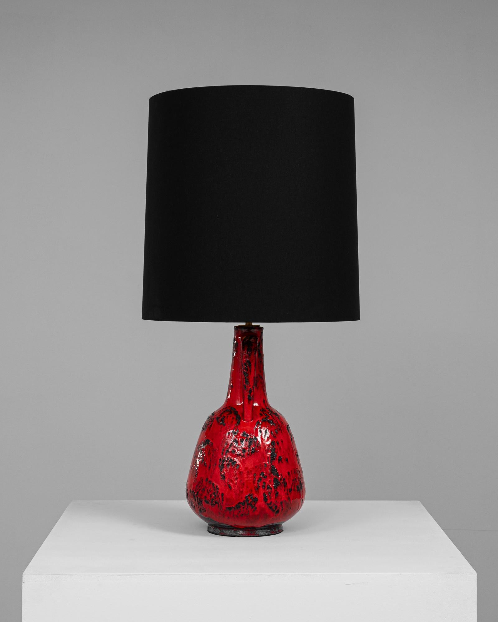 Cette étonnante lampe de table en céramique allemande est une pièce d'apparat du 20e siècle. Le glaçage rouge audacieux de la lampe, accentué par de riches motifs texturés noirs, exsude le style moderne du milieu du siècle, tandis que sa forme