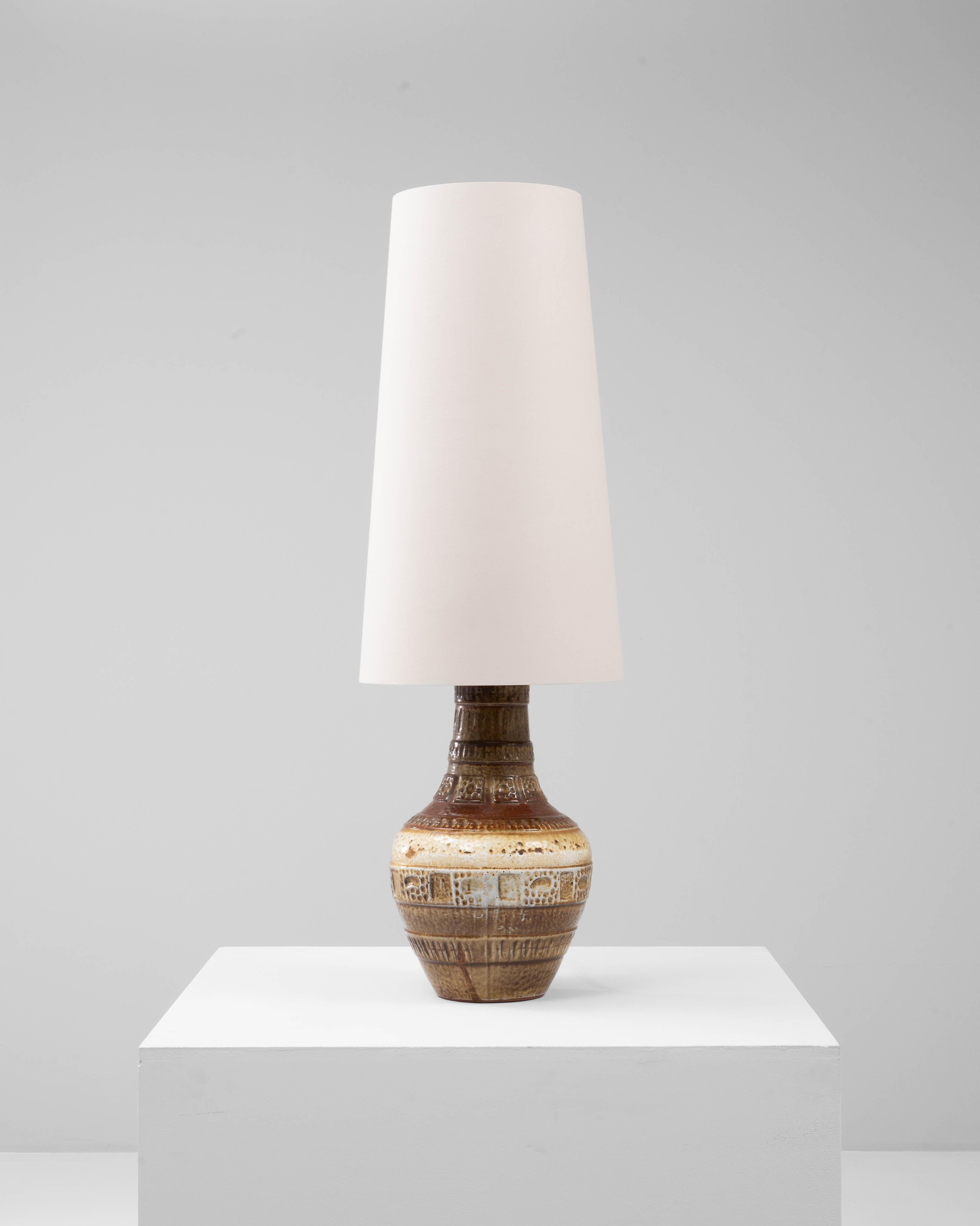 Cette lampe de table en céramique allemande du XXe siècle présente une surface richement texturée et richement détaillée qui reflète l'artisanat de la poterie ouest-allemande du milieu du siècle dernier. Inspirée d'une forme de cruche