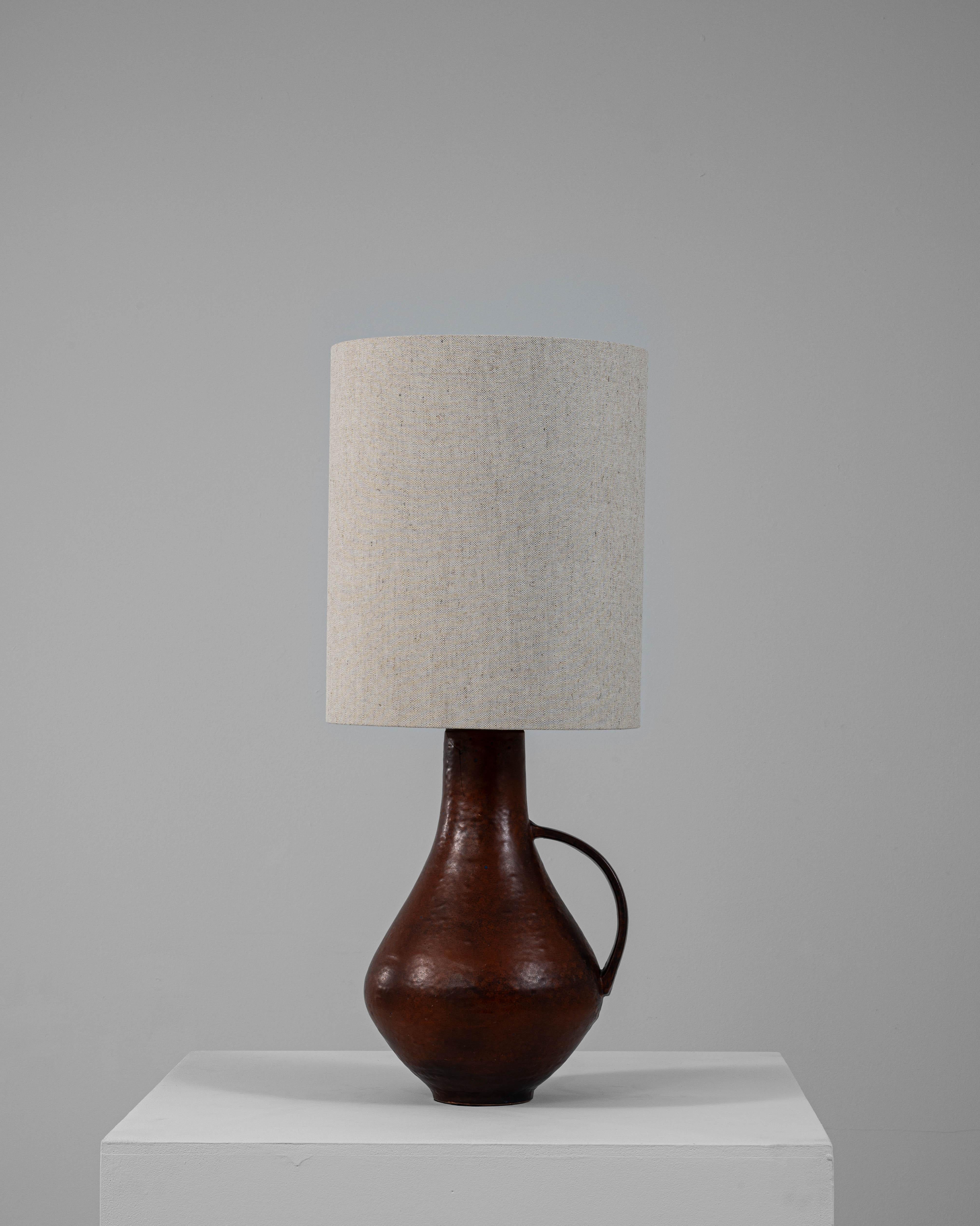 Cette lampe de table en céramique allemande du 20e siècle présente une riche glaçure brun terre et une silhouette intemporelle en forme de cruche dotée d'une seule poignée sculptée. Le col allongé et la base bulbeuse évoquent les formes