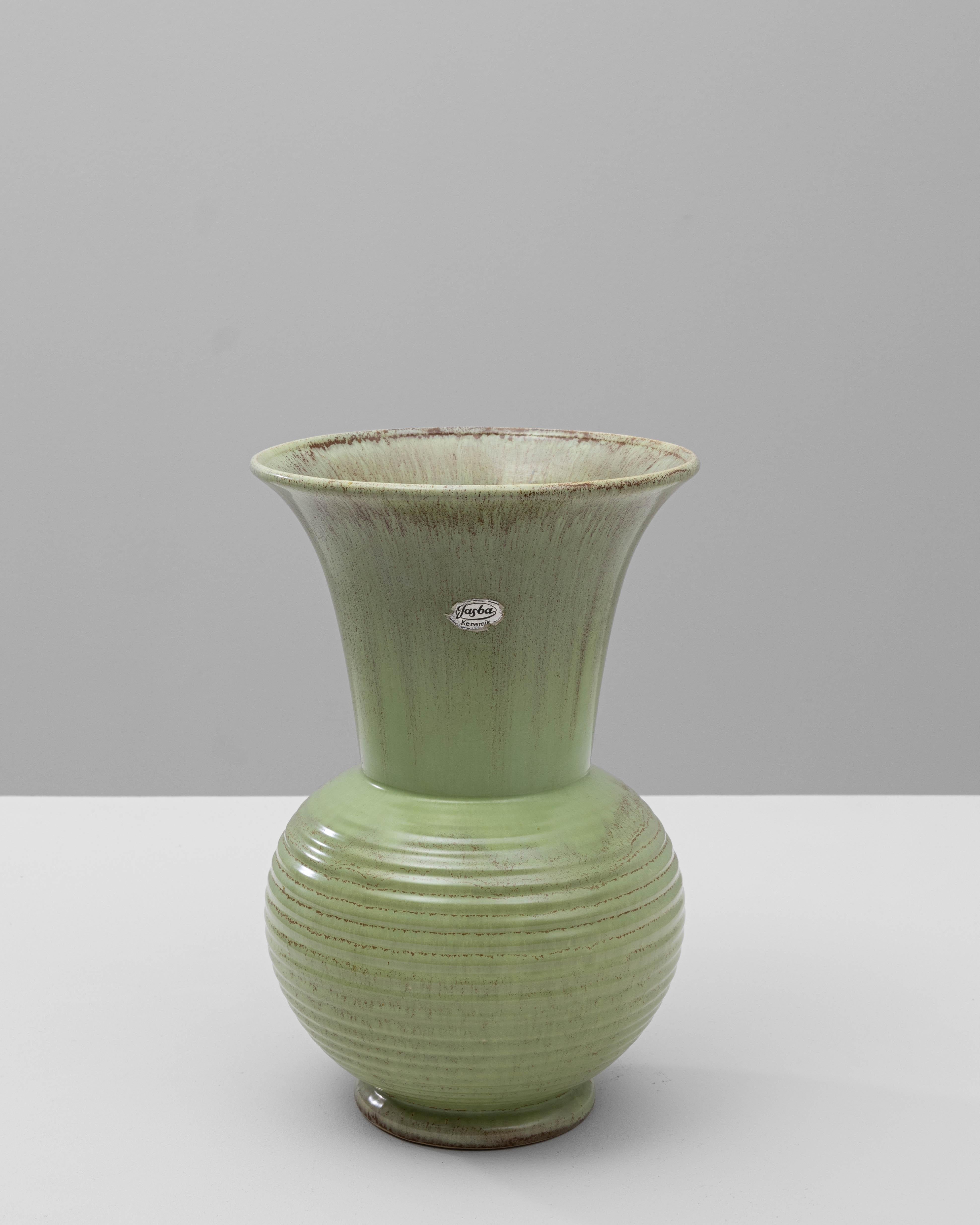 Questo squisito vaso in ceramica tedesca del XX secolo incarna una miscela armoniosa di forma e funzione. Il suo collo graziosamente svasato si trasforma in una base arrotondata, offrendo una silhouette senza tempo che mette in mostra l'abilità