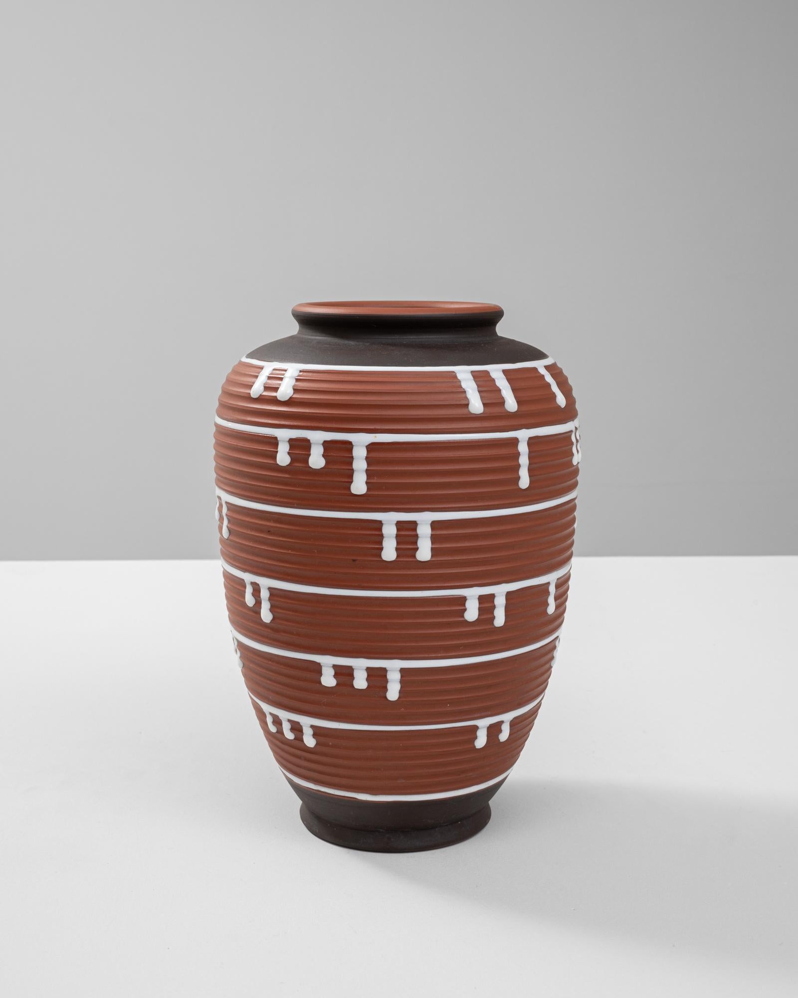 Questo vaso in ceramica tedesca del XX secolo esemplifica l'estetica audace e artistica del design di metà secolo. Il corpo color terracotta è ornato da creste orizzontali, che creano uno sfondo testuale per il sorprendente smalto bianco a goccia