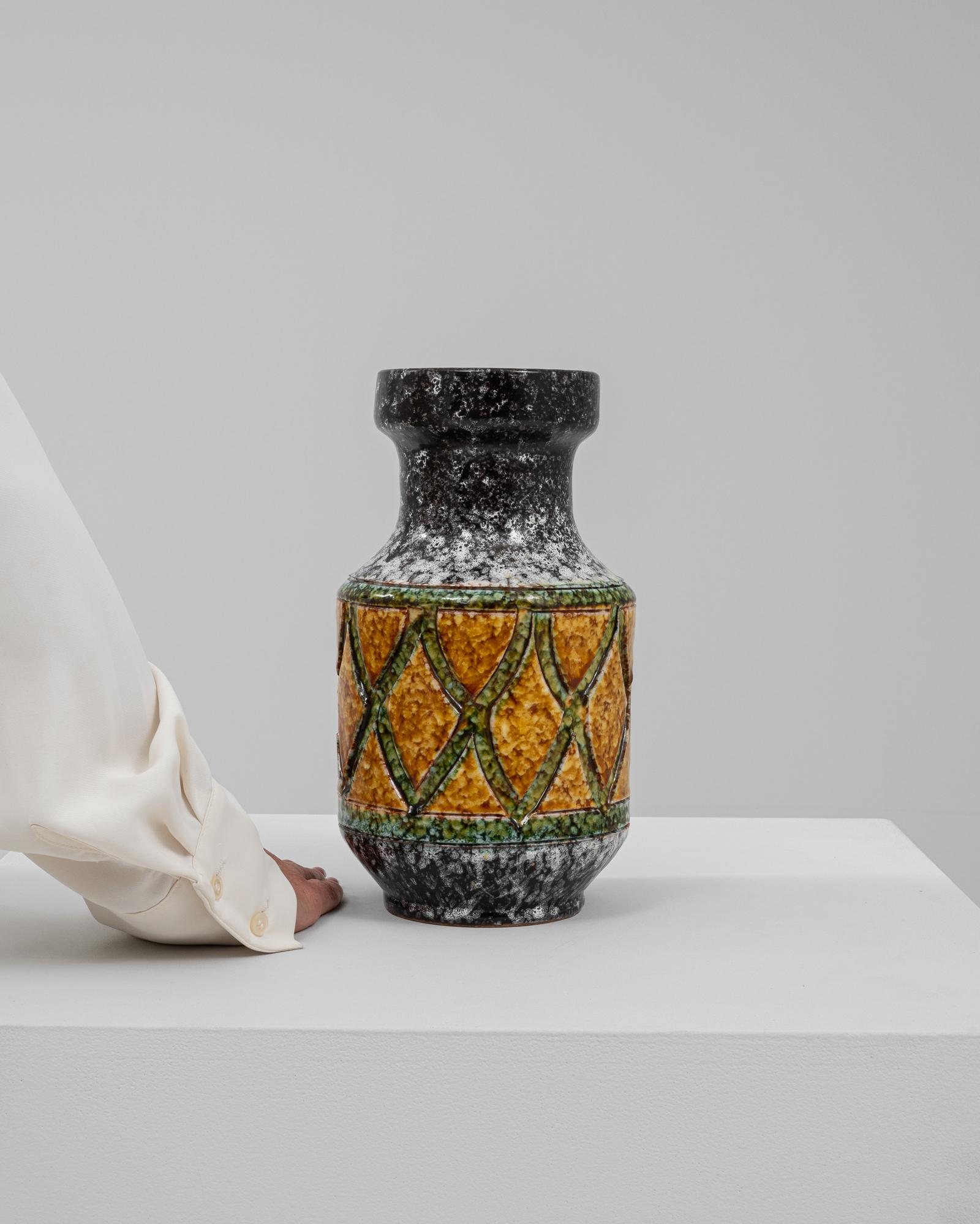 Questo vaso in ceramica tedesca del XX secolo è uno splendido esempio di design moderno di metà secolo con un'estetica audace e strutturata. L'intricato motivo di rombi smaltati gialli e verdi intrecciati contrasta meravigliosamente con lo sfondo