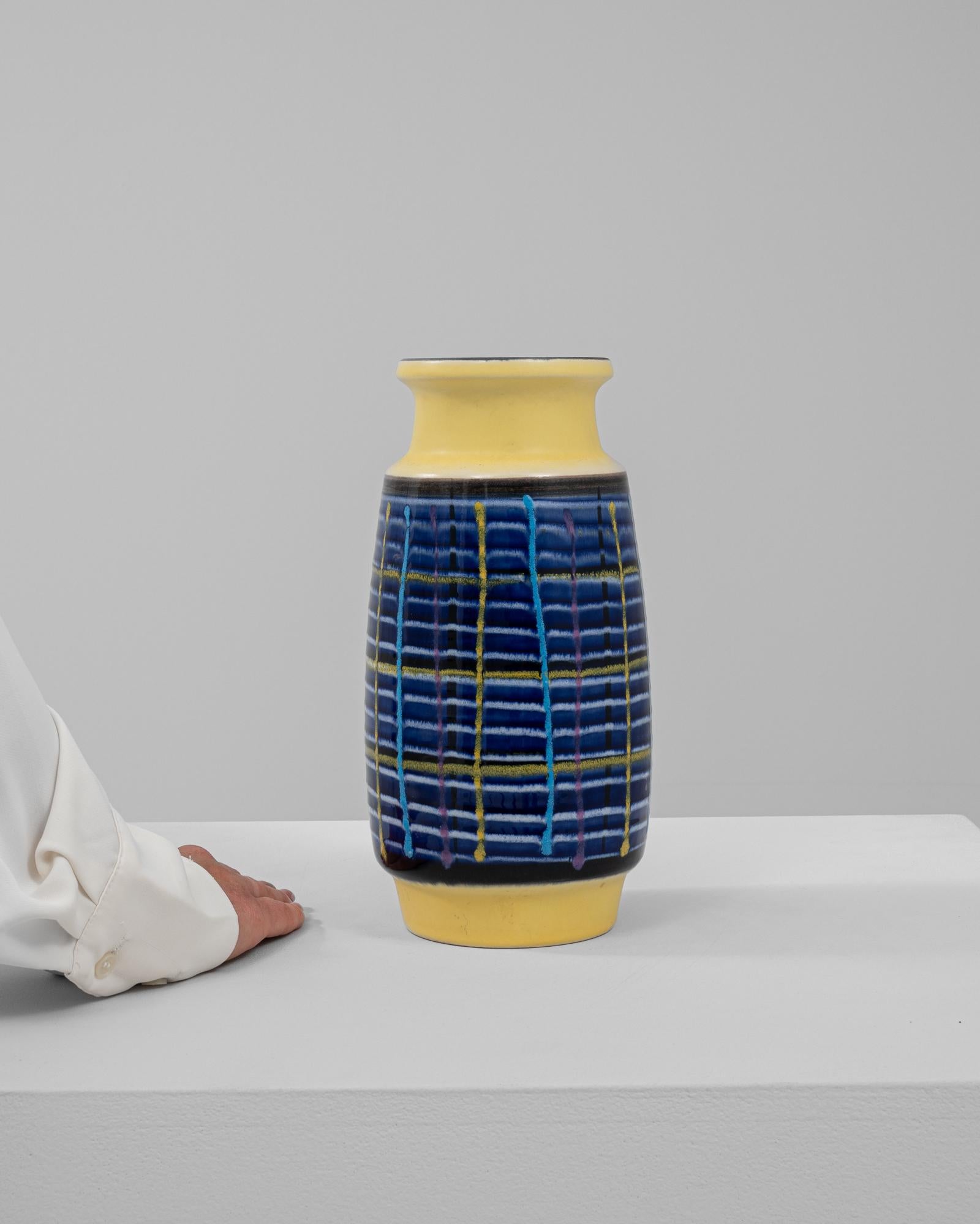Questo vivace vaso in ceramica tedesca del XX secolo è un pezzo forte che riflette l'arte moderna della metà del secolo. Il suo design dinamico presenta un motivo a griglia in blu, giallo e rosa vivaci su uno sfondo blu intenso, creando un contrasto