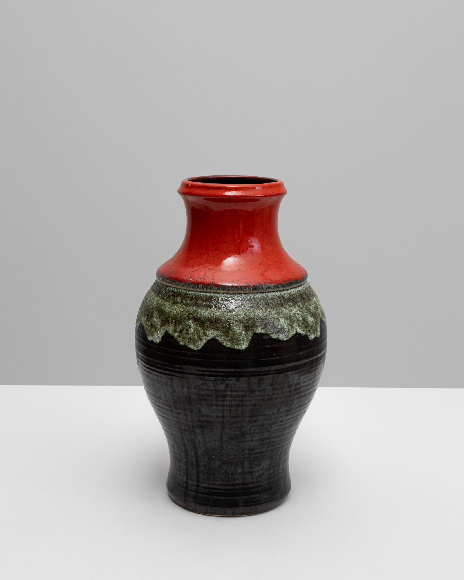 Questo vaso in ceramica tedesca del XX secolo incarna l'estetica audace ed espressiva della ceramica europea di metà secolo. Caratterizzato da una composizione dinamica dello smalto, passa da un collo rosso lucido a una fascia verde strutturata che
