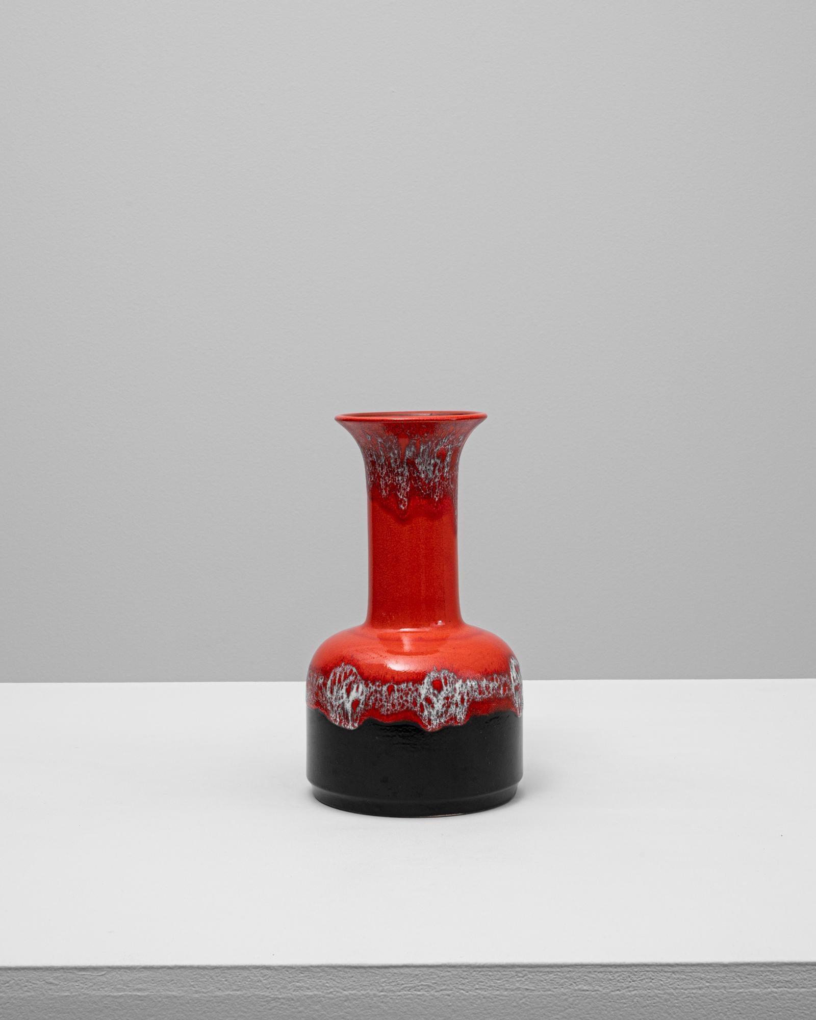 Este jarrón de cerámica alemana del siglo XX encarna el atrevido arte de la época moderna de mediados de siglo. Su distintiva silueta presenta un cuello cilíndrico que se ensancha en una base redondeada, acabada en un llamativo esmalte rojo que pasa