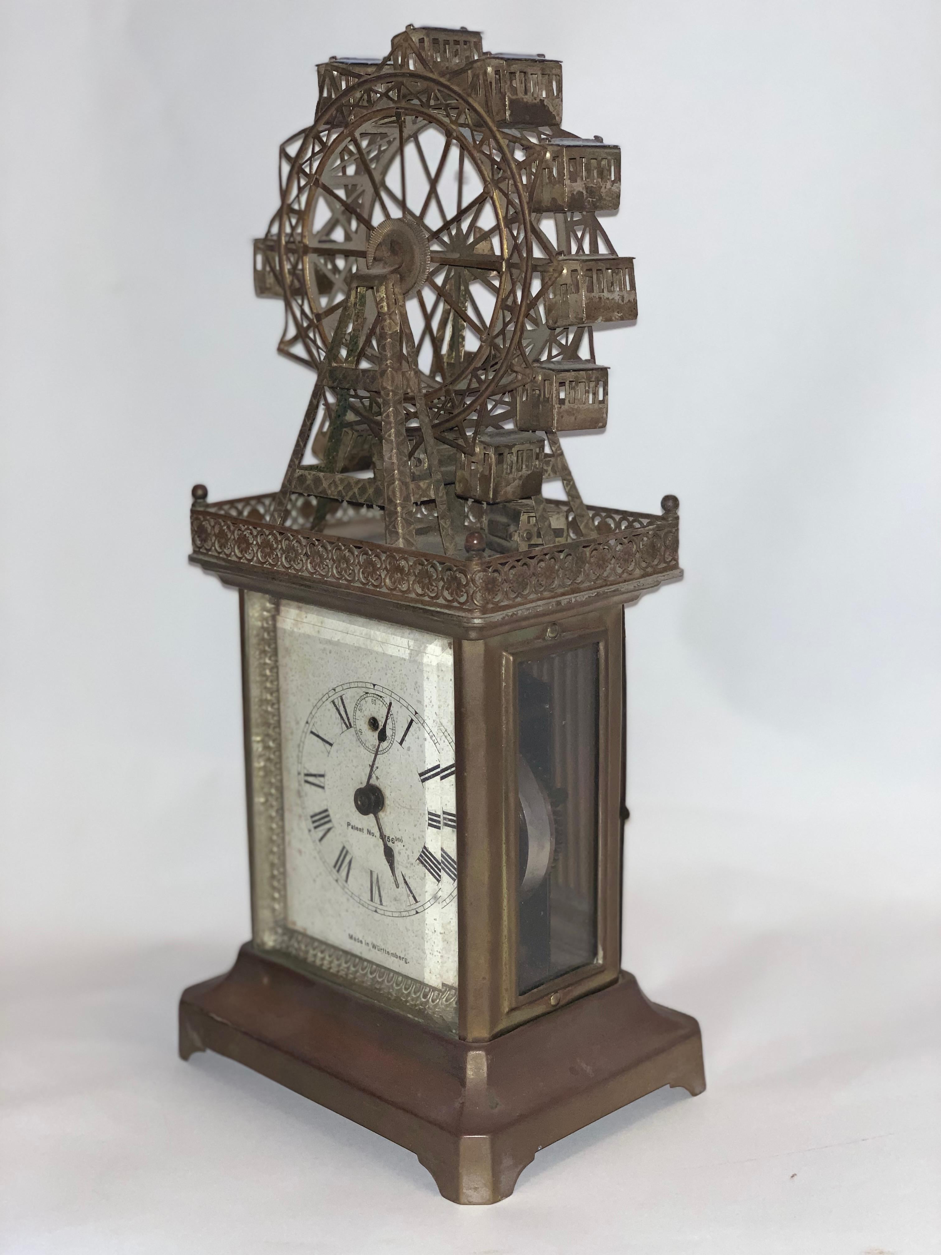 Pendule de calèche du début du 20e siècle avec automate de grande roue. Cadran romain blanc avec cadran secondaire des secondes sur un motif de flèches croisées, et cadran secondaire de l'alarme en chiffres arabes, surmonté de l'inscription 