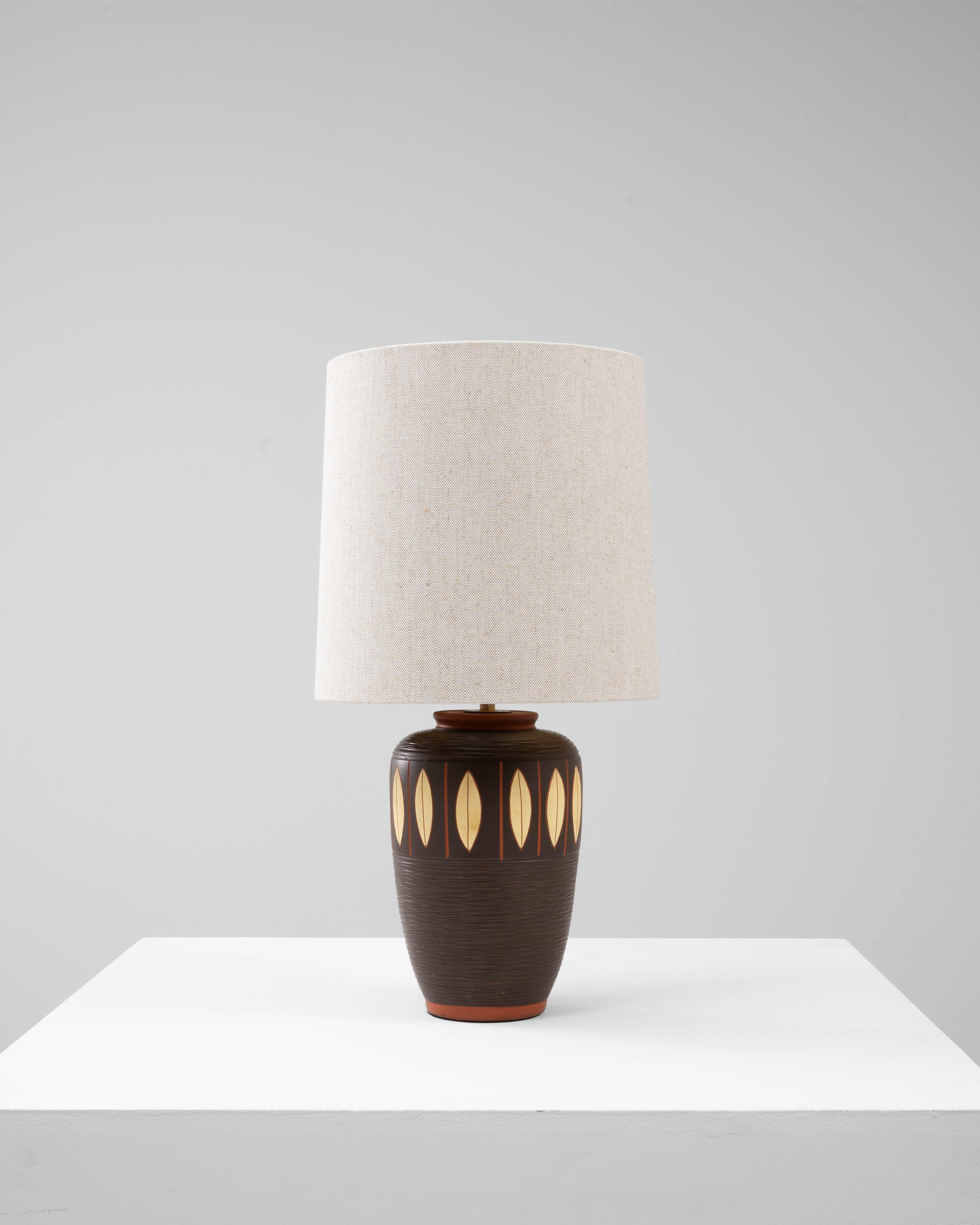 Cette lampe de table géométrique en céramique allemande du 20e siècle allie une forme sculpturale à des détails décoratifs raffinés. La base présente une riche glaçure brun foncé avec une surface subtilement texturée, créant une profondeur et un