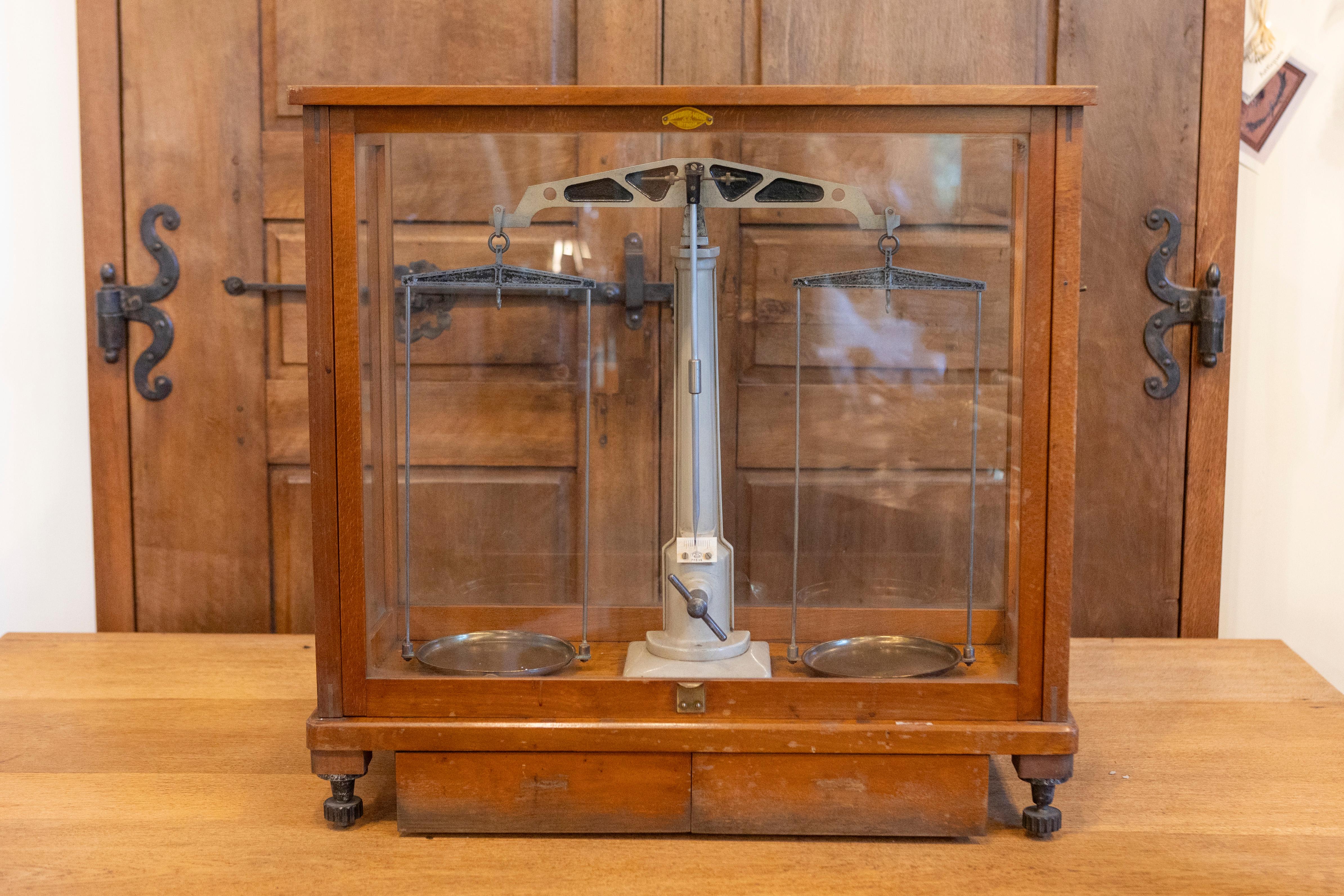 Cette balance allemande du XXe siècle, enfermée dans un cadre de verre et de bois, est un bel exemple d'ingénierie de précision et de conception fonctionnelle. La balance est dotée d'un boîtier en bois poli magnifiquement travaillé, avec des