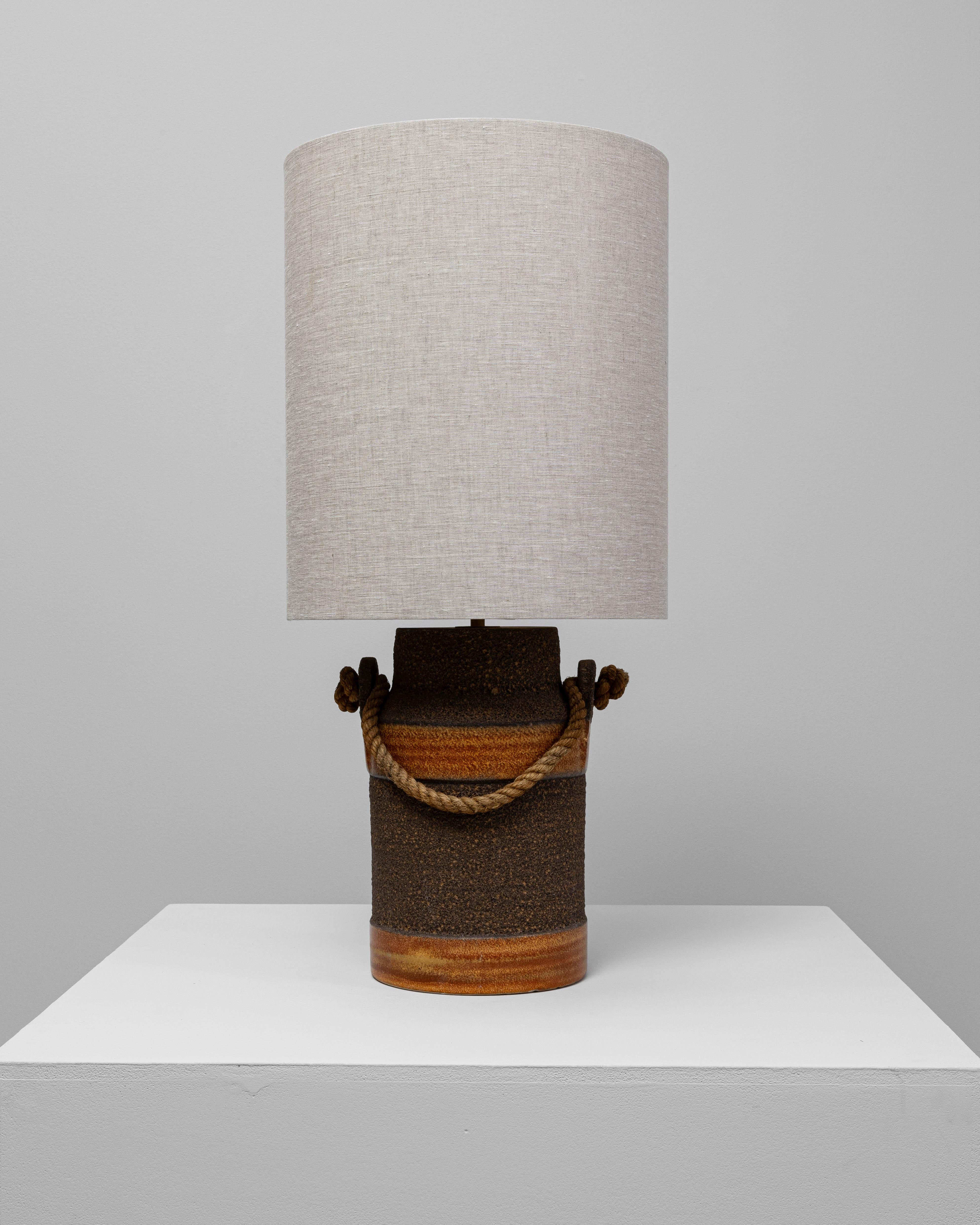 Cette lampe de table allemande du 20e siècle en céramique orange avec poignée en corde allie le charme rustique à l'artisanat du milieu du siècle. La base cylindrique en céramique présente une surface richement texturée, accentuée par un émaillage