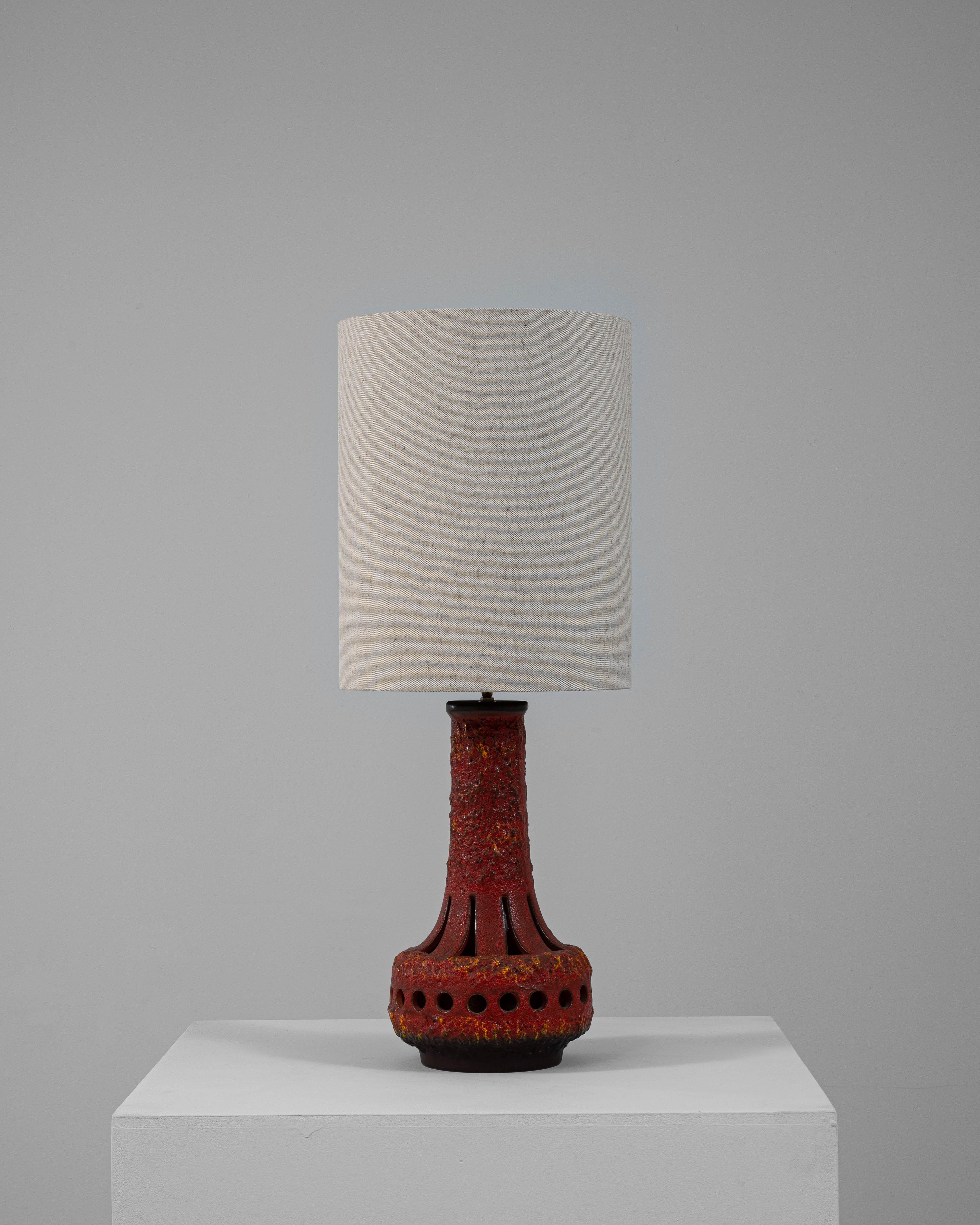 This 20th-century German ceramic table lamp features a striking pierced design with a red Fat Lava glaze, celebrated for its richly textured, volcanic surface. The cylindrical form flares into a bold, rounded base adorned with evenly spaced circular
