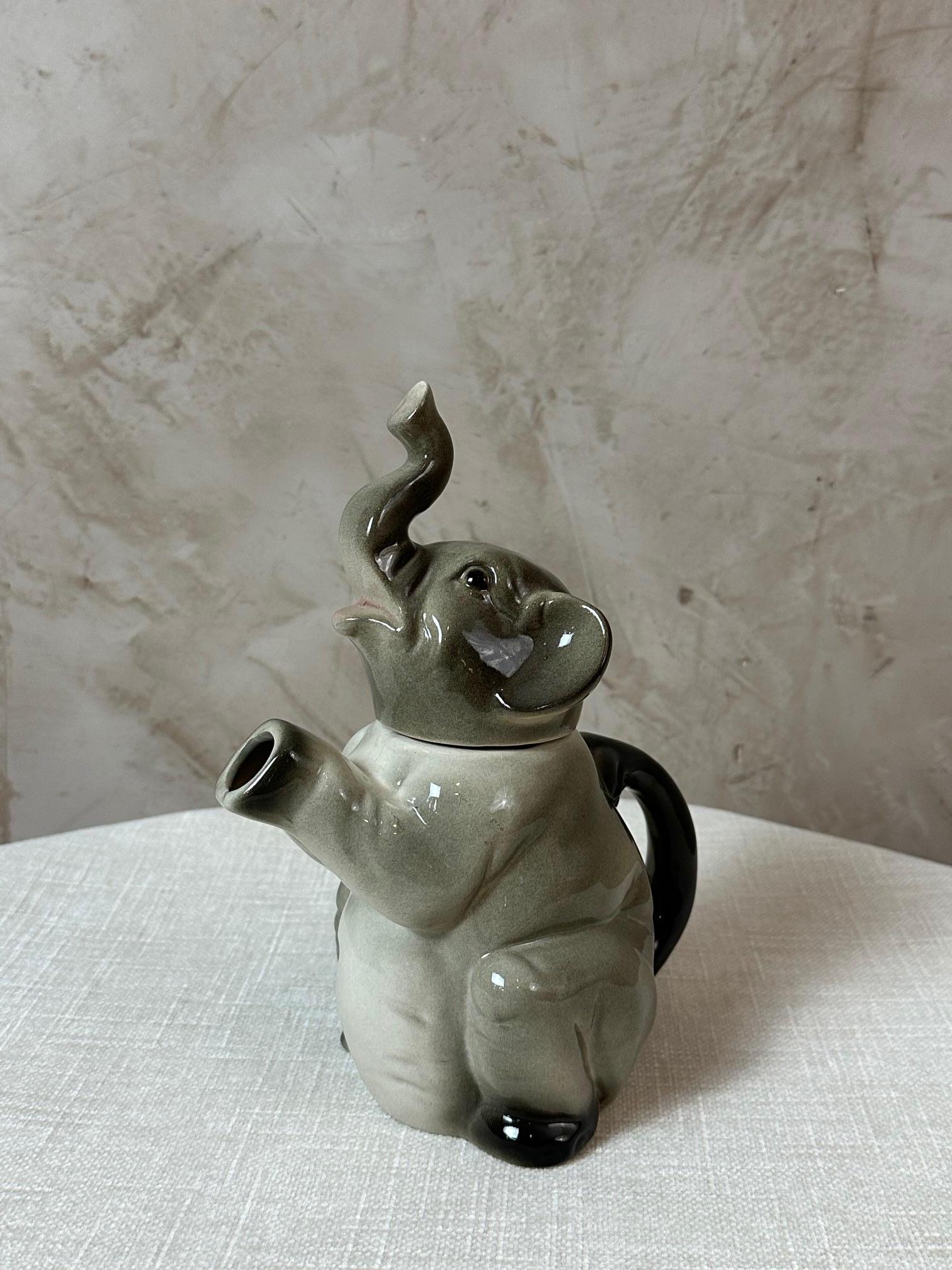 Graziosa teiera in ceramica che raffigura un elefante seduto con la proboscide sollevata, abilmente disegnata come beccuccio. Questo pezzo stravagante combina funzionalità e decorazione, rendendolo originale e invitante. Fabbrica tedesca Erphila.