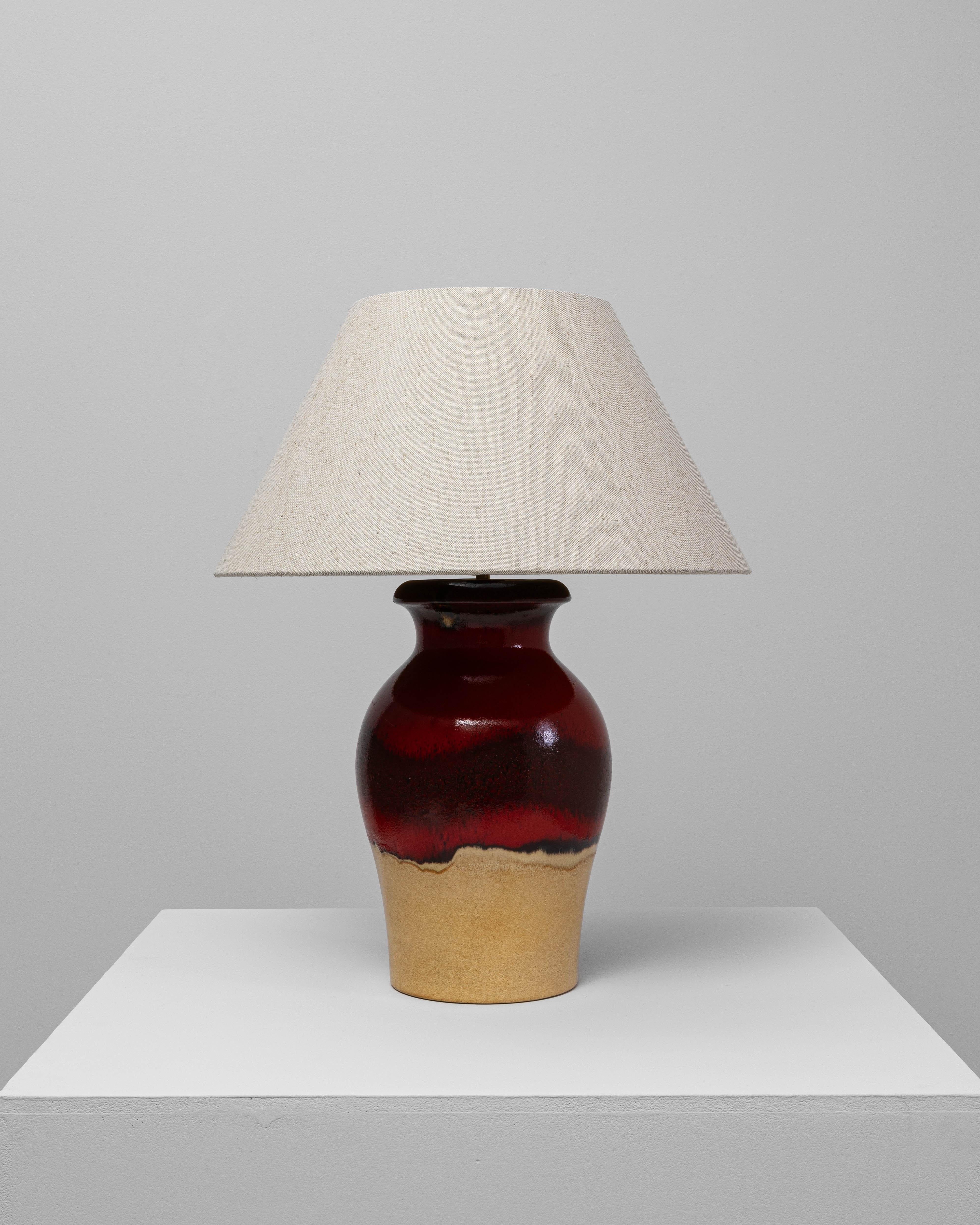 This 20th Century German red and tan ceramic table lamp features a striking two-tone glaze that blends rich color with organic texture. The upper portion showcases a deep, glossy red with subtle black mottling, creating a dynamic, flowing surface