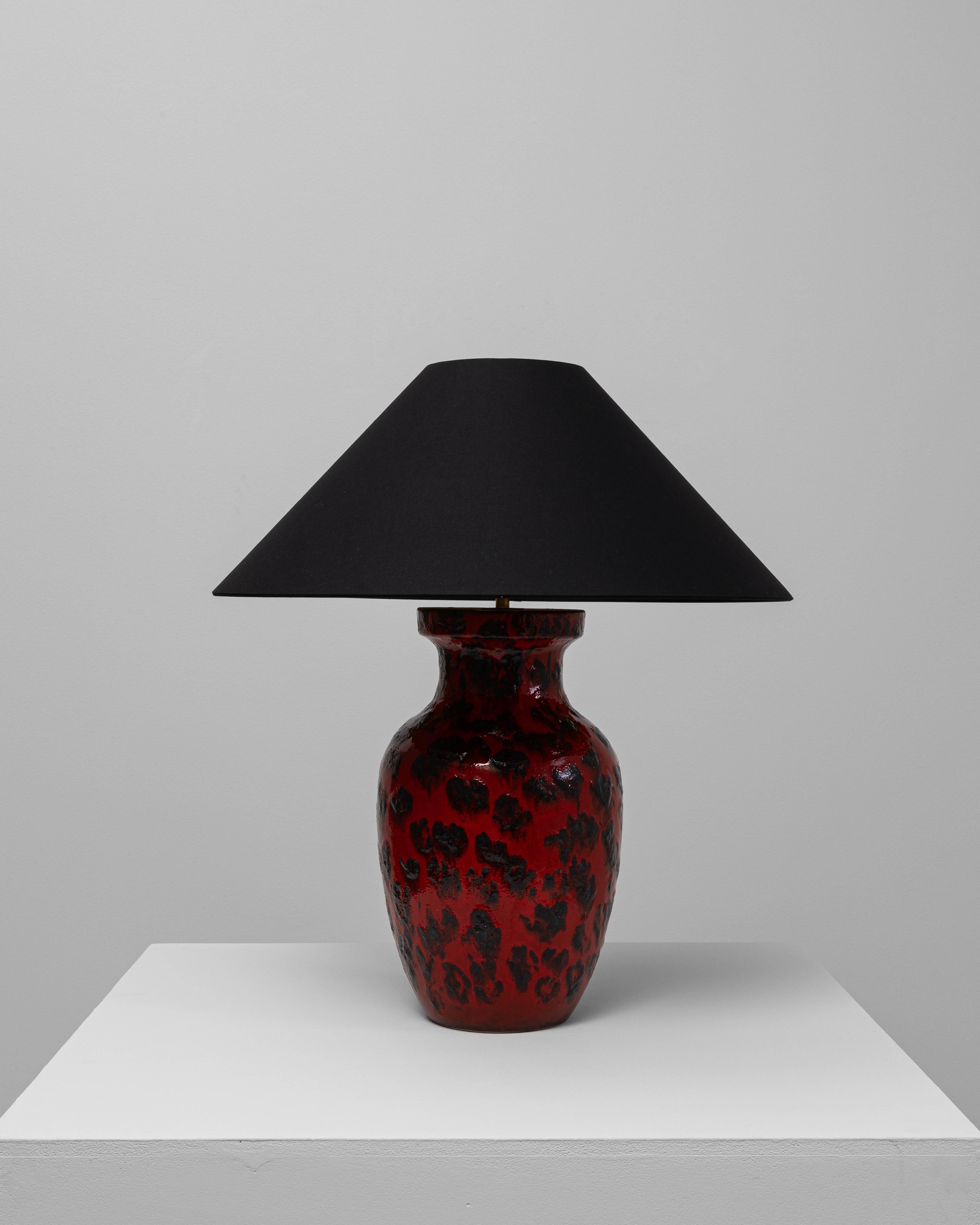 Cette lampe de table en céramique rouge allemande du 20e siècle présente une présence audacieuse et sculpturale définie par sa glaçure vive et sa texture de surface expressive. La base en forme de récipient est finie dans un ton rouge profond avec