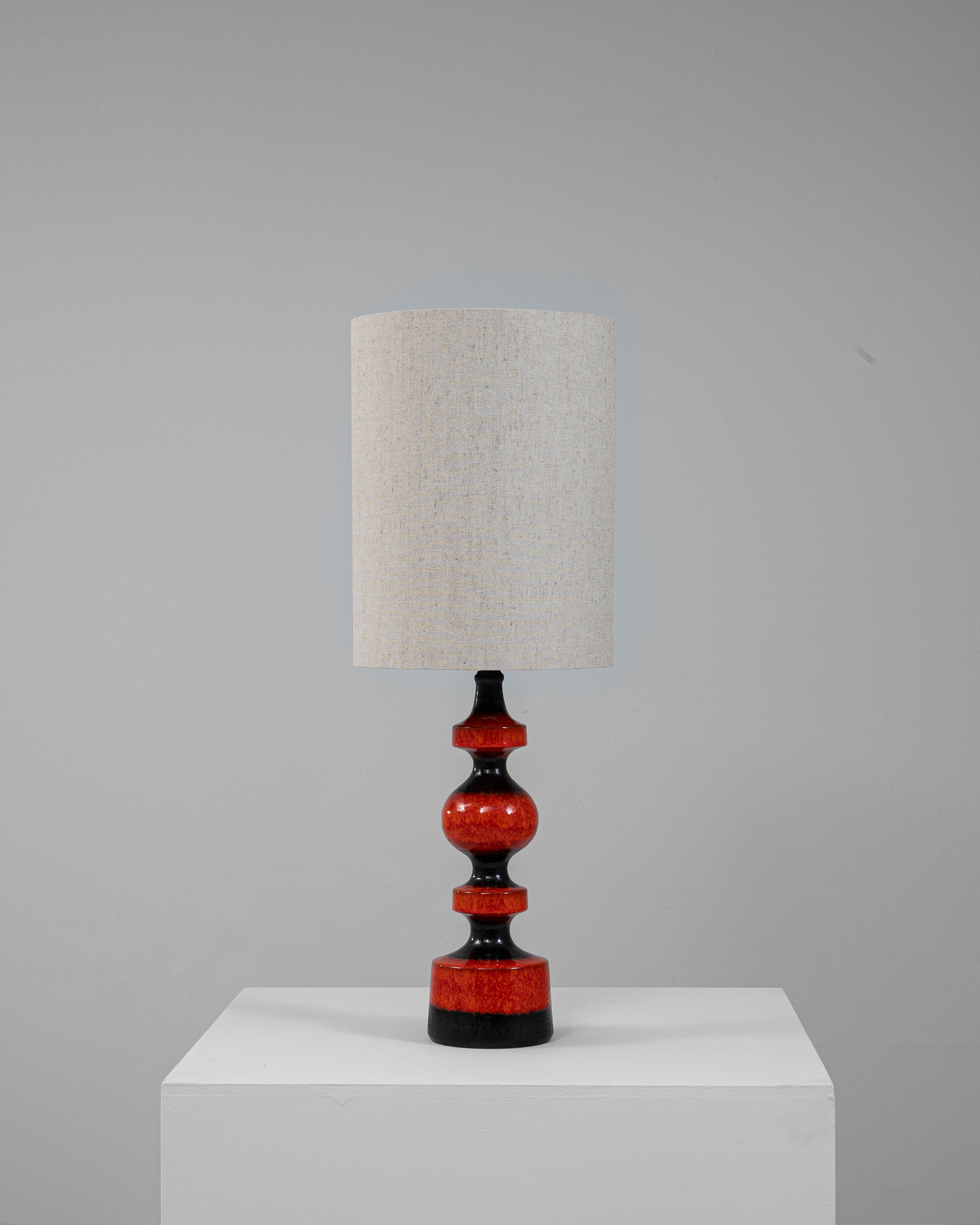 This striking 20th-century German table lamp showcases the bold aesthetic of mid-century ceramic design with a vibrant red lava glaze. The sculptural base features a curvaceous, geometric silhouette finished in deep red tones with black accents,