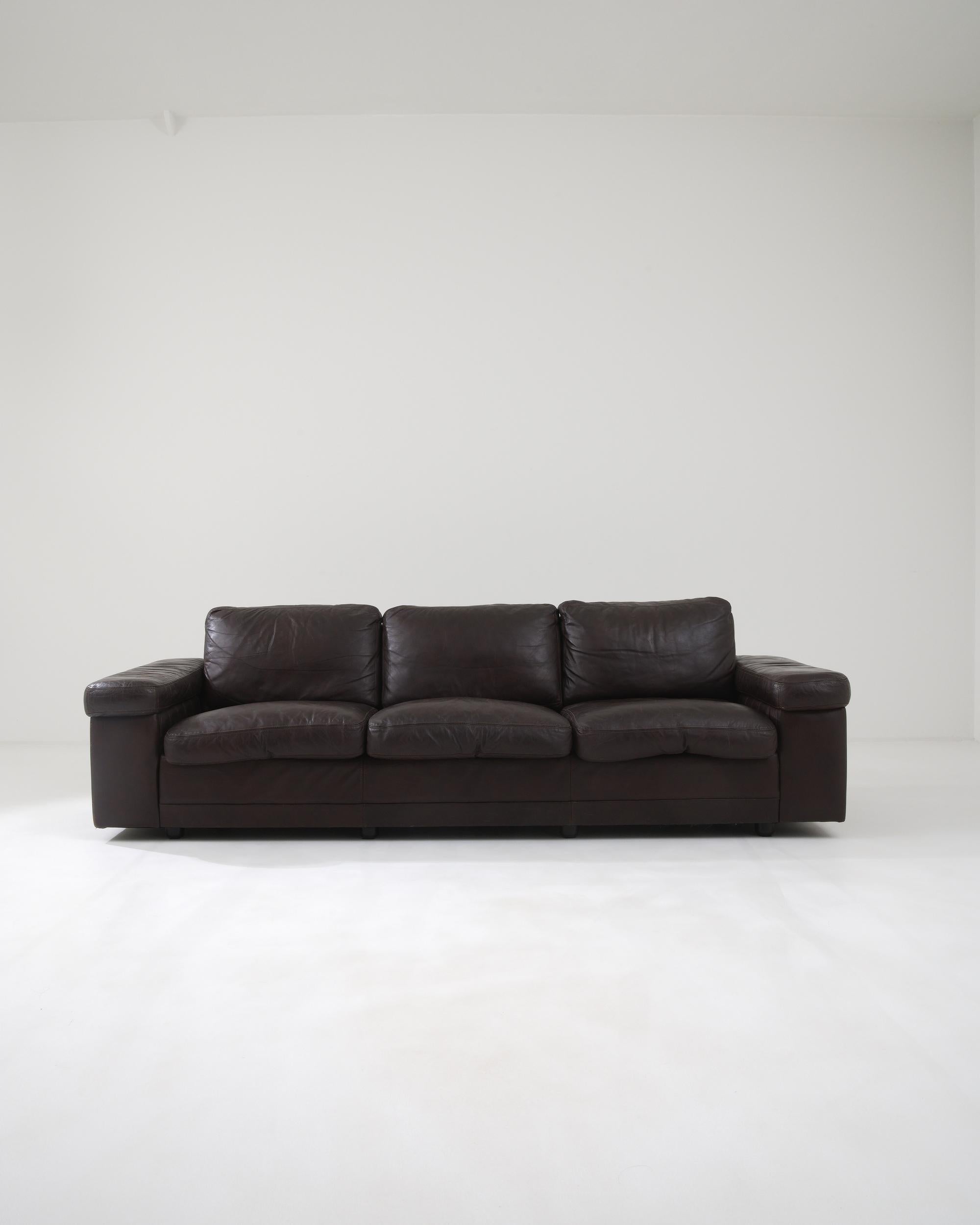 Dieses elegante Dreisitzer-Sofa wurde im 20. Jahrhundert in Deutschland hergestellt und strahlt eine klassische Ausstrahlung aus. Die weichen, mit luxuriösem, dunkelbraunem Leder umhüllten Kissen werden von breiten, geometrischen Armlehnen gestützt