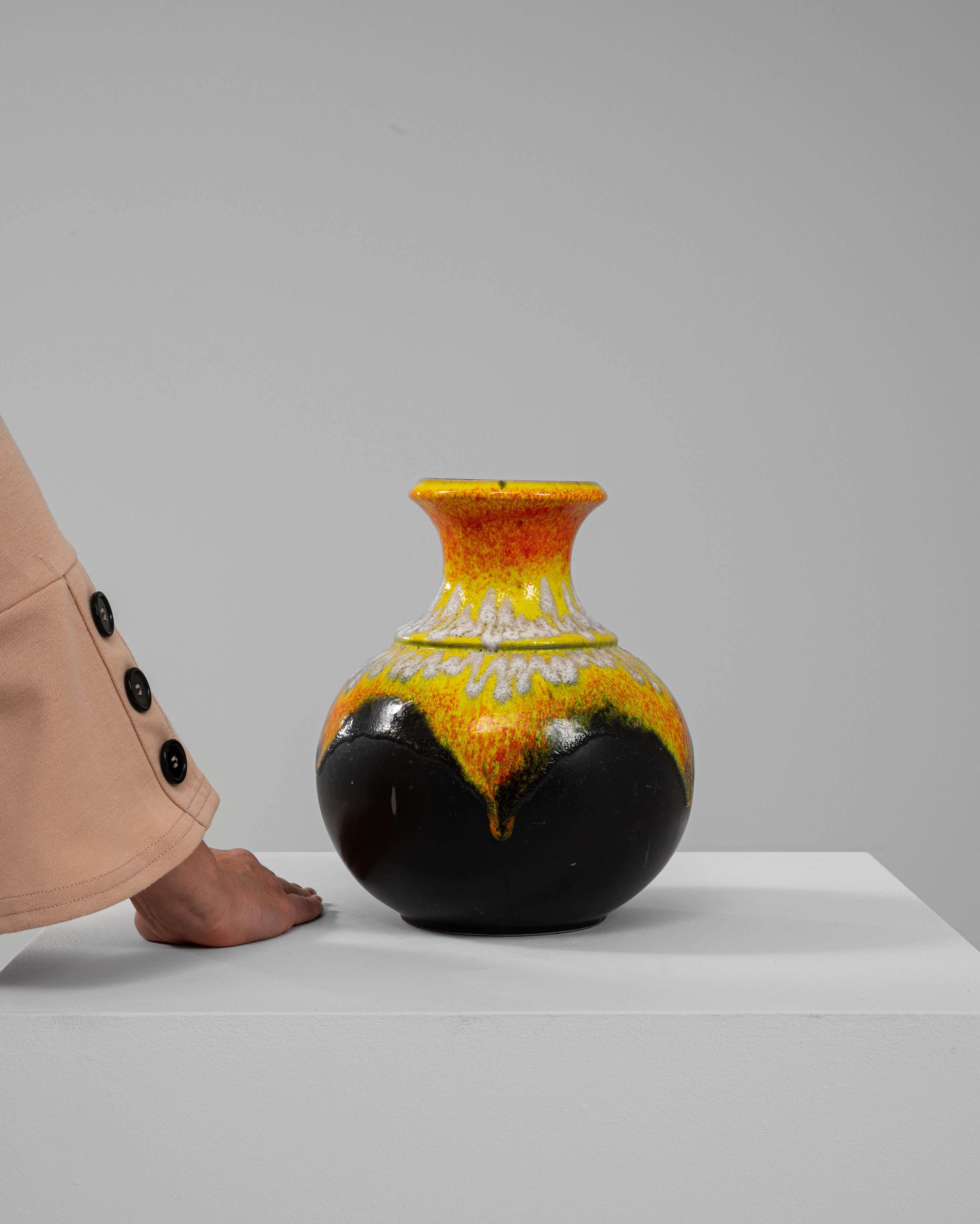 Este llamativo jarrón de cerámica de Alemania Occidental del siglo XX es un cautivador ejemplo del emblemático estilo de esmalte de lava. El atrevido diseño presenta un vibrante degradado de amarillo fuego y naranja en la parte superior, con una