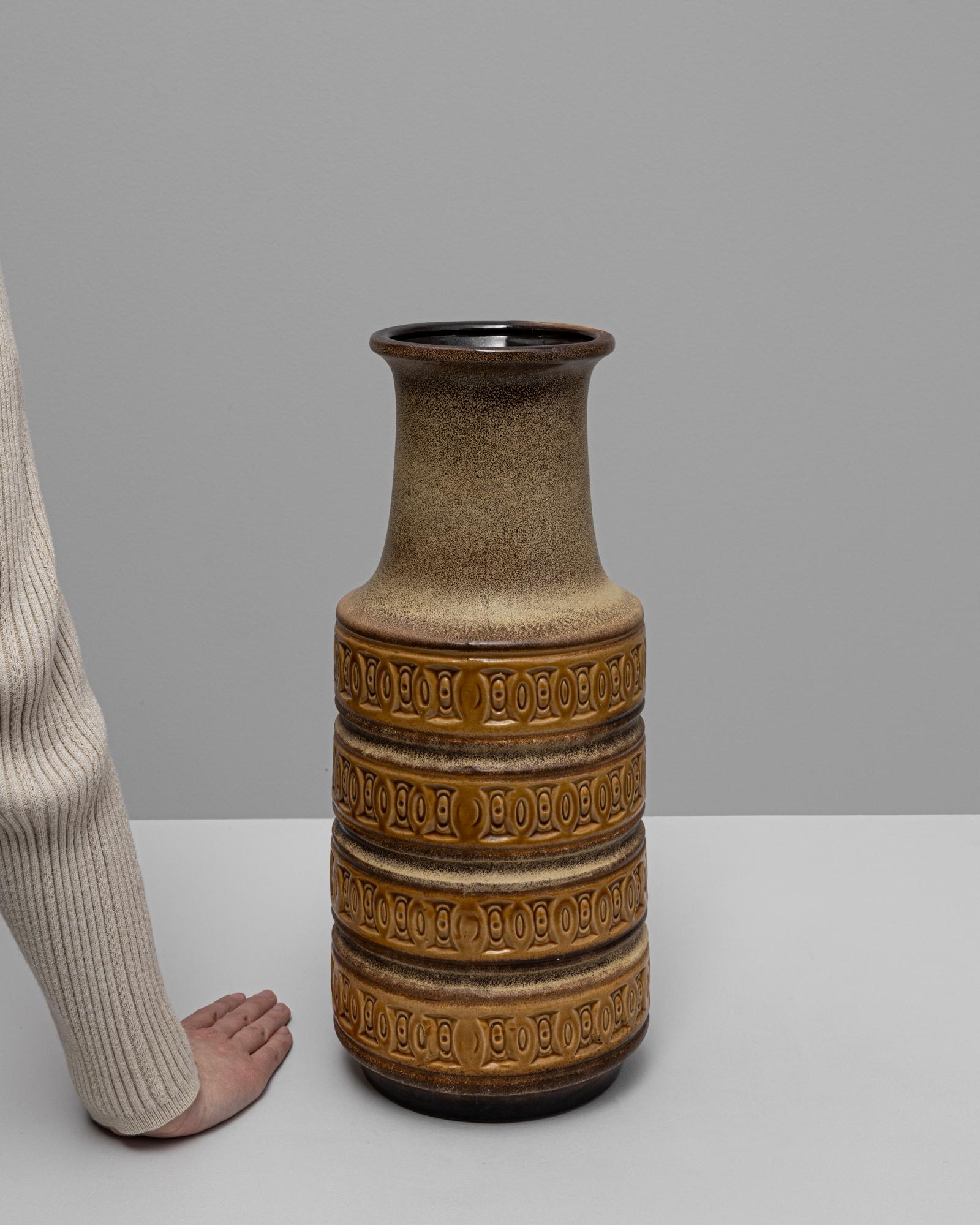 Exemple frappant du design ouest-allemand du milieu du siècle dernier, ce vase en céramique du XXe siècle présente une haute forme cylindrique avec une poignée géométrique audacieuse et un relief en bandes rythmées. La surface texturée combine des