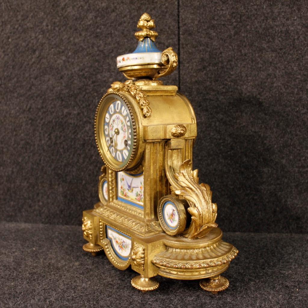 French clock from the mid-20th century. Object in gilded and chiselled bronze and brass, adorned with hand-painted ceramic elements with floral decorations of great pleasure. Rear door with glass to be replaced (see photo), mechanism not working, to