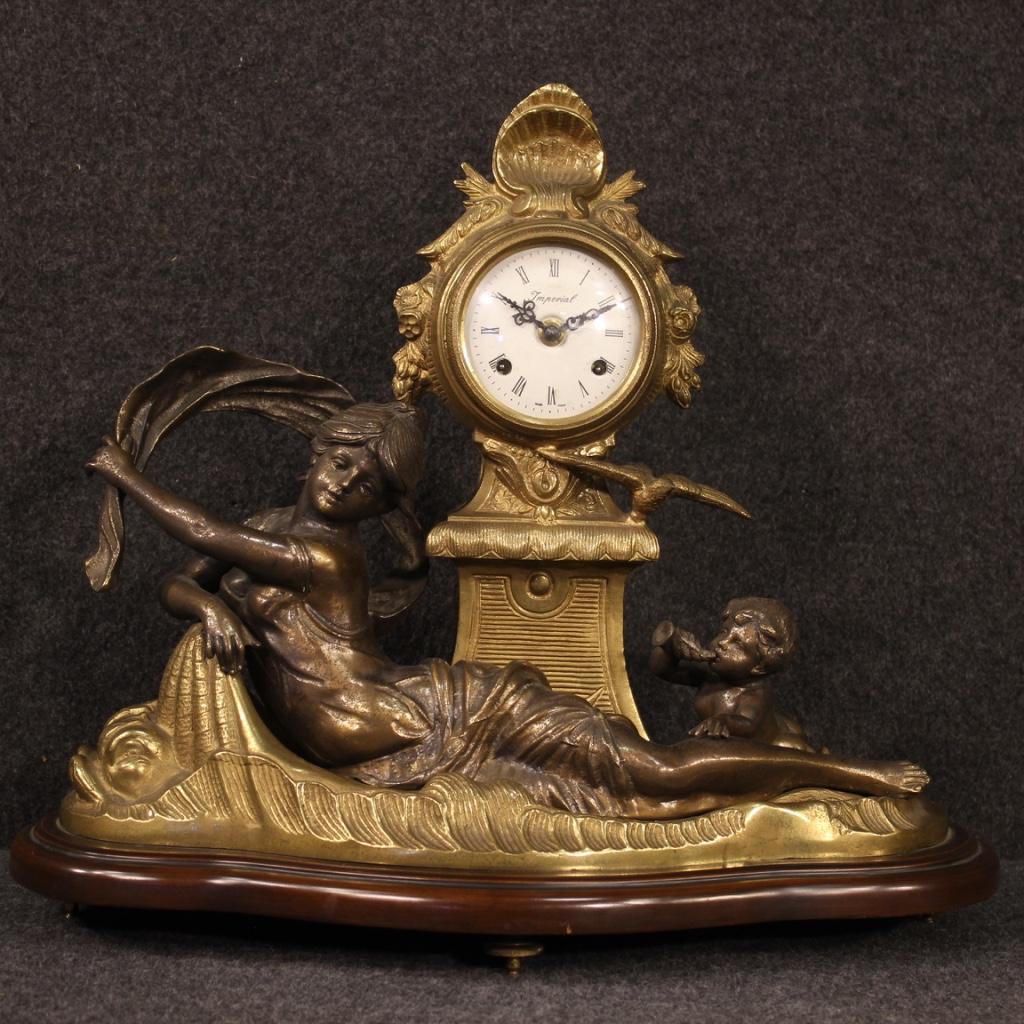 French clock from the first half of the 20th century. Gilt bronze and antimony object, patinated and chiseled adorned with sculptures, mahogany-colored lacquered wooden base. Clock supported by four feet positioned under the base, of good solidity.