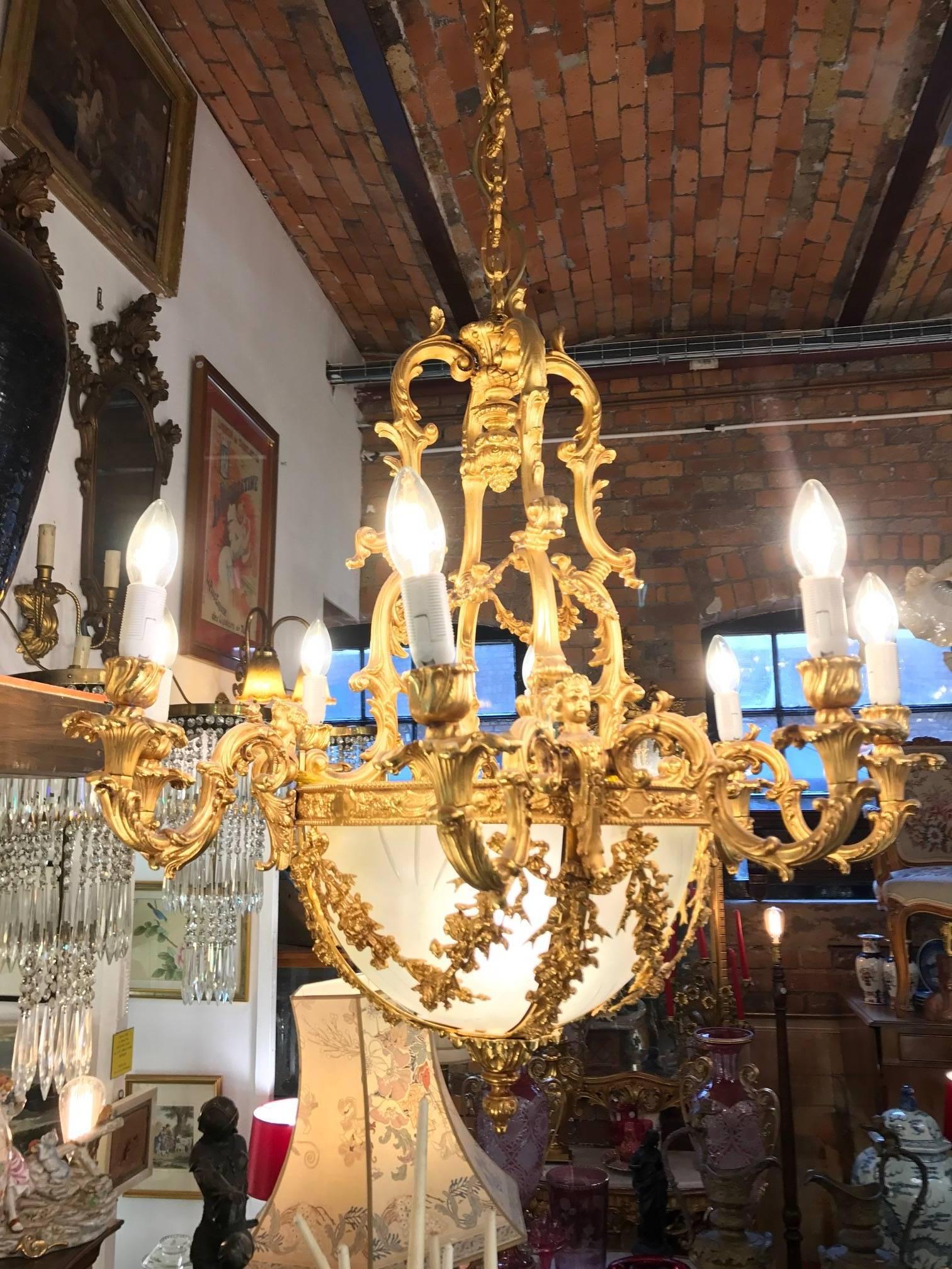 20th century gilt bronze chandelier in Louis XVI style with eight scrolled branches. The arms of the chandelier coil out from a frosted, hand cut, oval crystal bowel base. Decorated with a gilt bronze frieze of Greek waves, cherub faces, leaves and