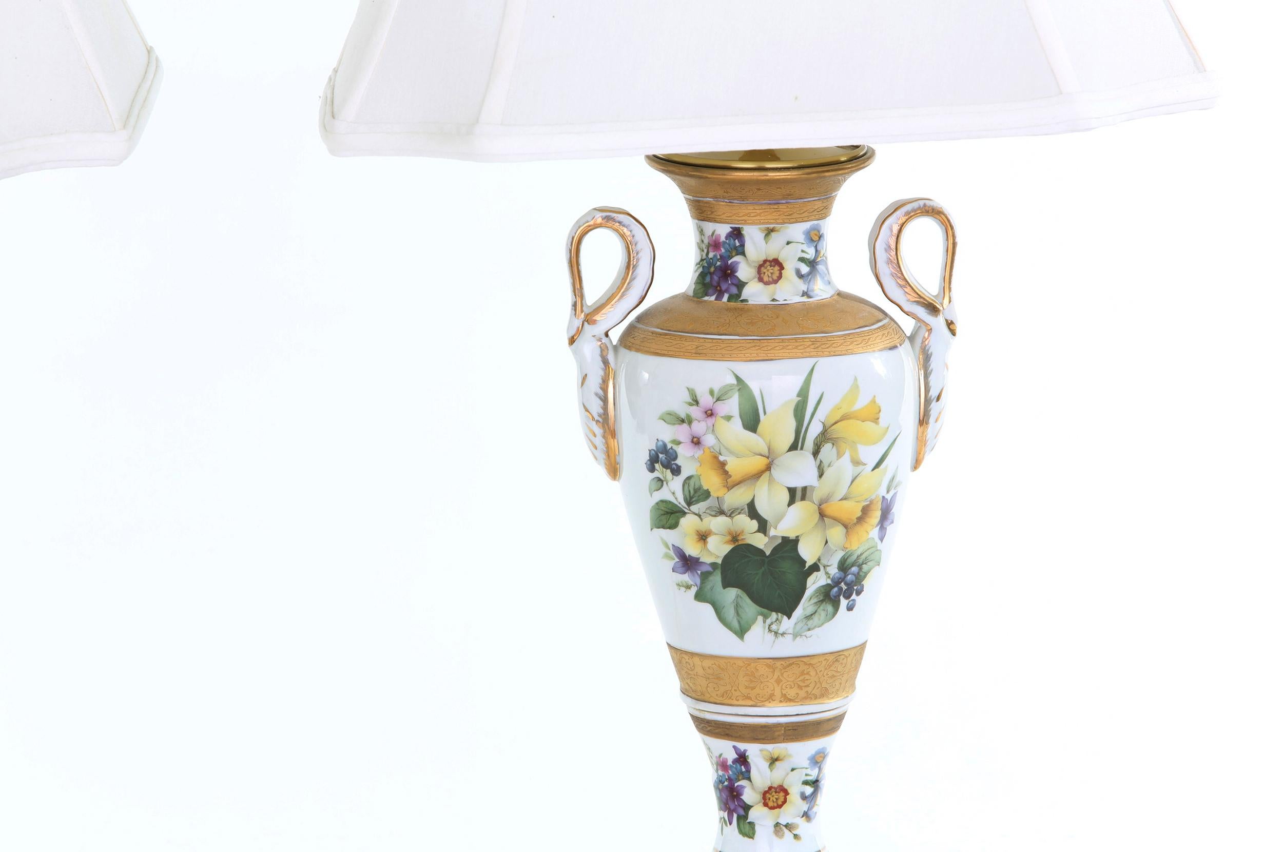 Early 20th century porcelain pair of table lamps with exterior gilt and painted floral design details. Each lamp is in good working condition. Minor wear consistent with age / use. Each lamp stand about 28 inches tall x 7.5 inches diameter. Each