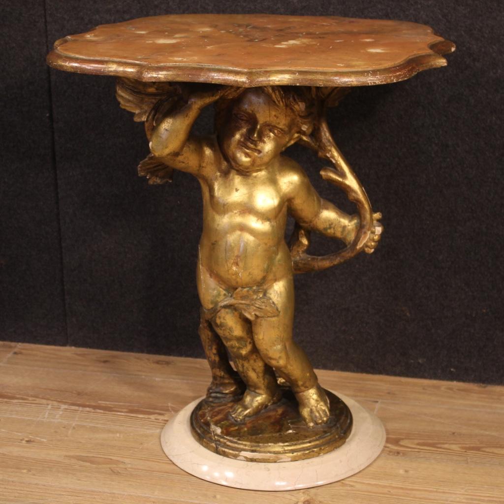 Italian coffee table from the mid-20th century. Furniture in carved and gilded wood with marble base adorned with large angel sculpture. Lacquered faux marble wooden top of good size and service. Furniture of excellent stability and solidity given