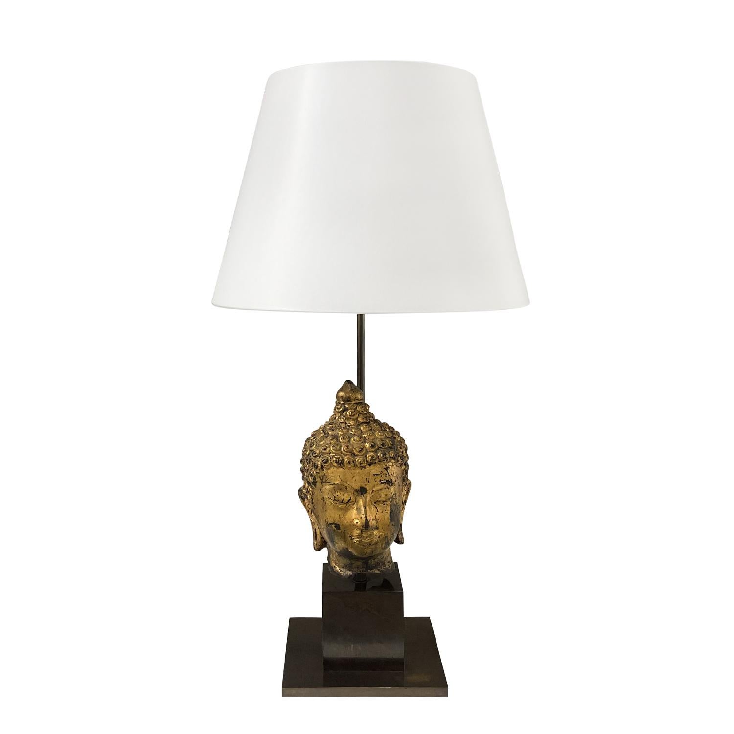 A late vintage Mid-Century Modern Asian Buddha table lamp with a new white round shade, made of hand crafted wood, in good condition. The detailed gold patinated head is supported by a rectangular metal base, featuring a one light socket. The wires