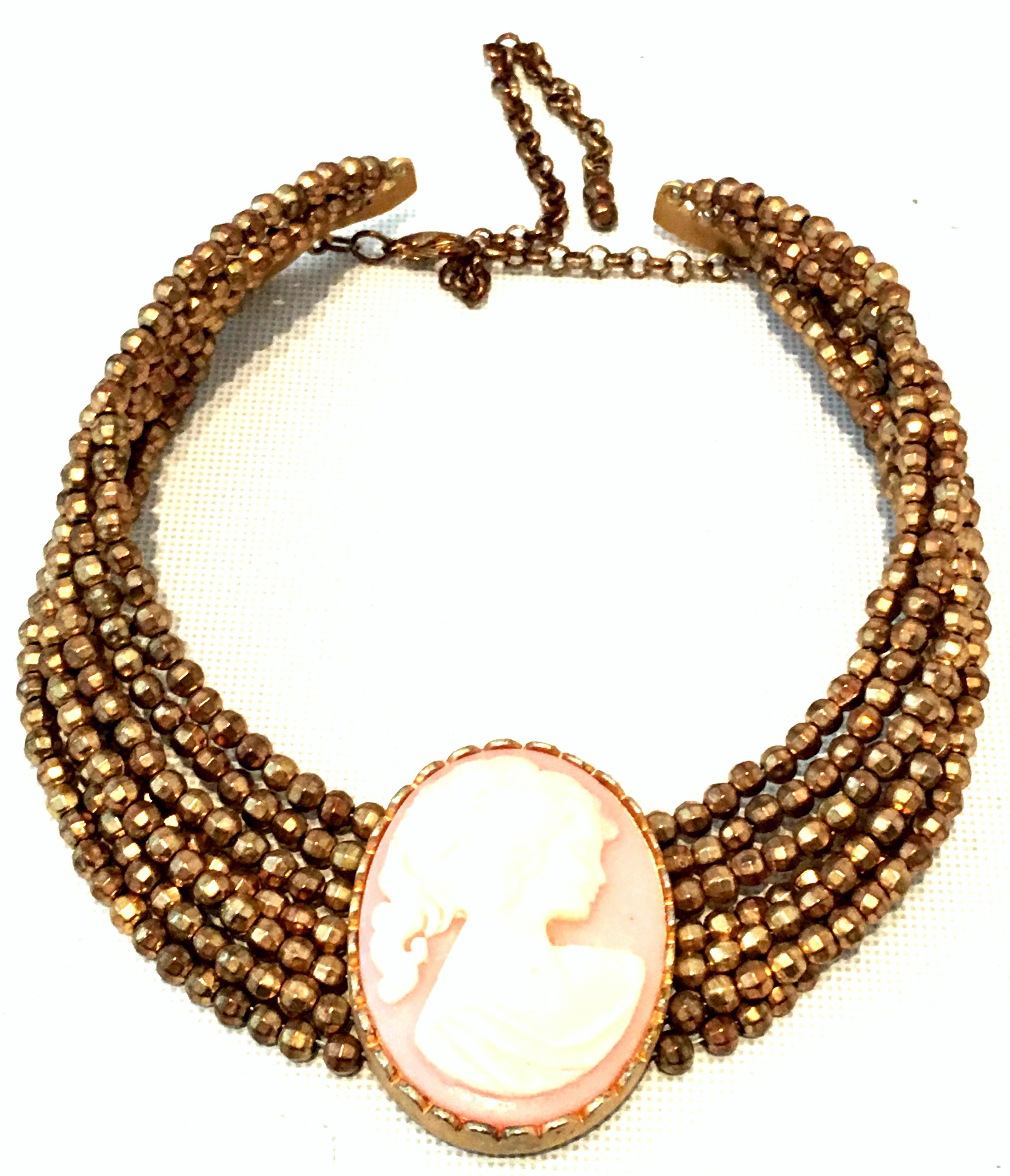 20th Century Gold Steel Cut Bead & Carved Lucite Cameo Multi Strand Choker Style Necklace. This finely crafted choker style necklace features seven rows of gold steel cut beads with a gold plate set Lucite carved pink and off white cameo central
