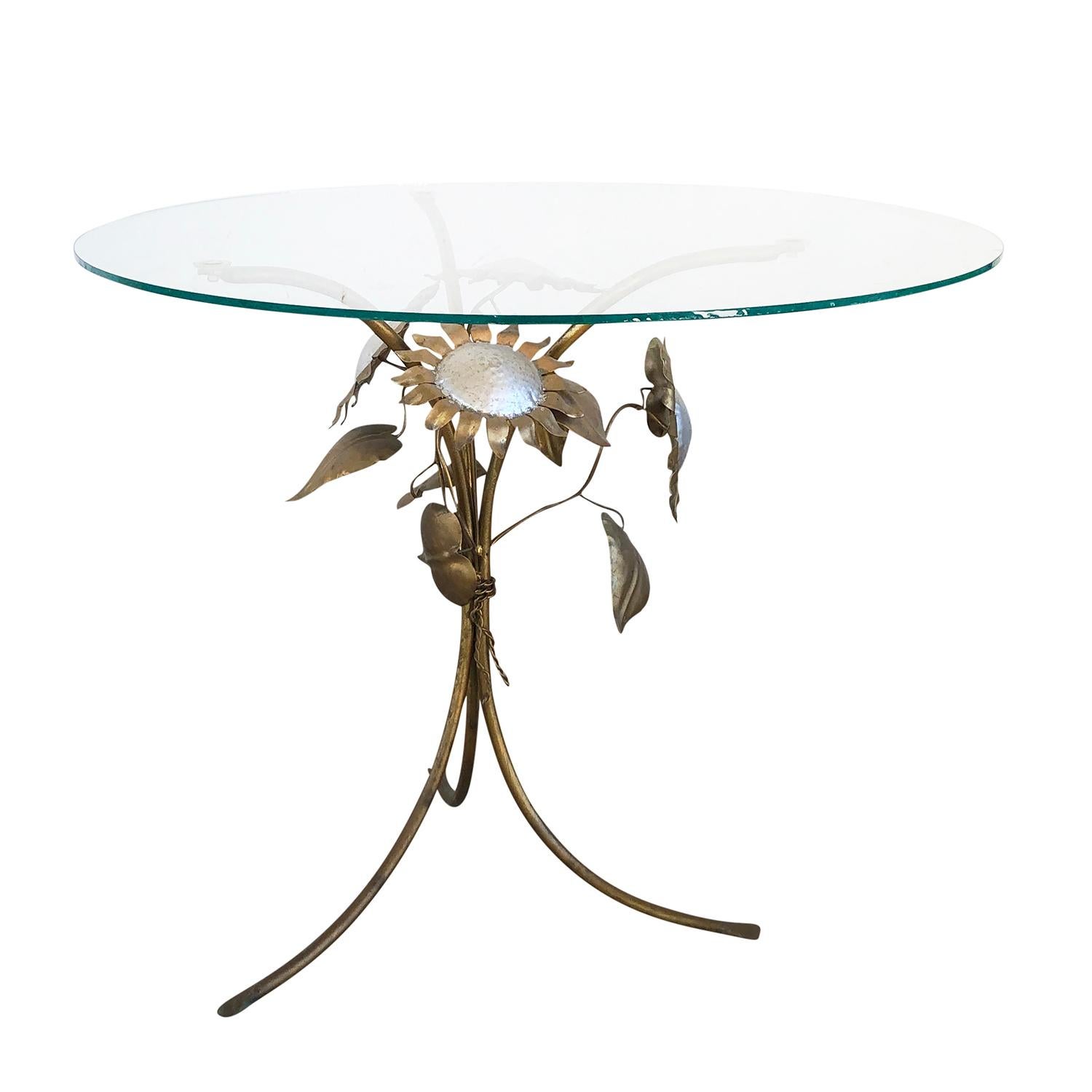 A gold, vintage Mid-Century Modern small round side, sofa table with a circular glass top and a gilded metal base on three legs and gracefully decorated with four metal sunflowers, in good condition. Wear consistent with age and use. Circa 1960,