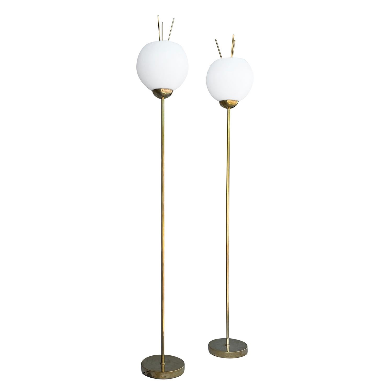 A gold, vintage Mid-Century Modern Italian pair of floor lamps made of hand crafted metal and brass, in good condition. The floor lamps are composed with a round white, frosted opaline glass shade, detailed with three feelers, featuring a one light