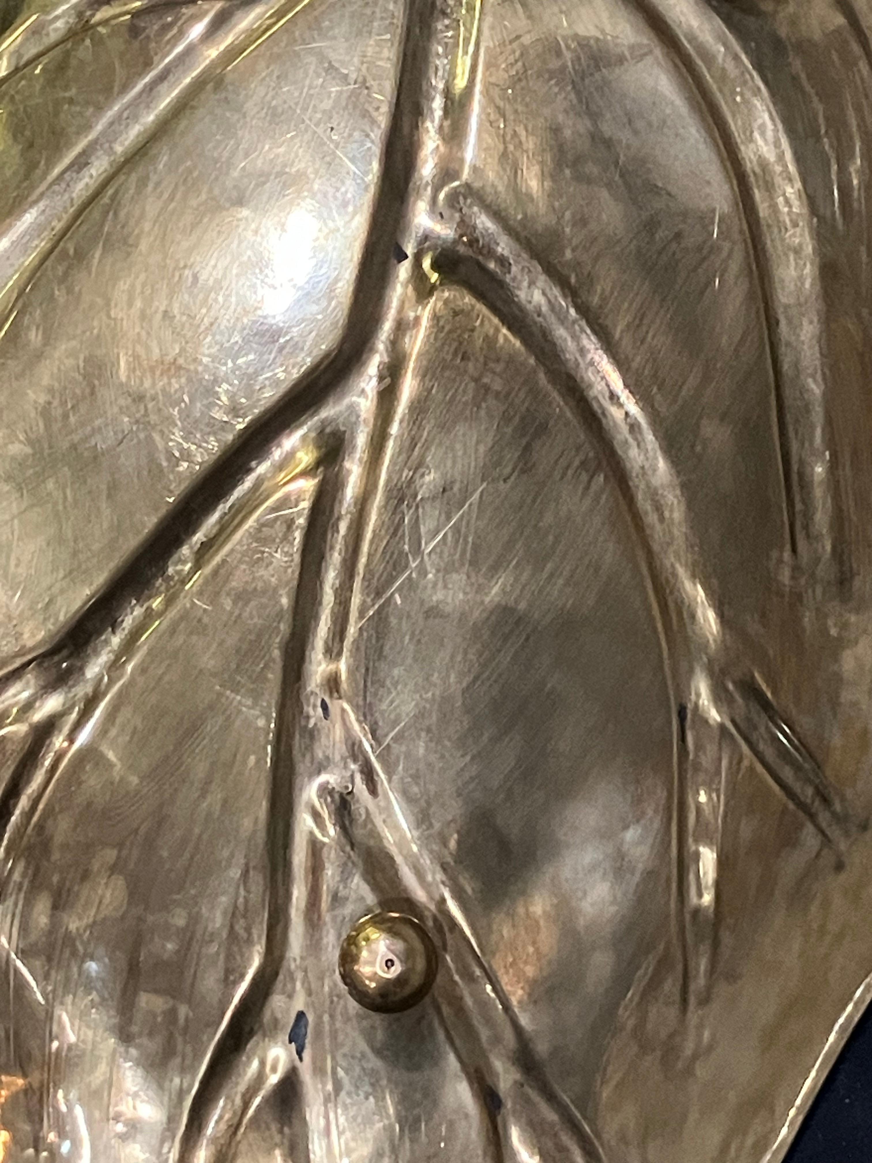 A 24-inch long dish shaped in the form of a stylized leaf with detailed veining. Finished in a reflective gold-tone surface, the piece features a gently curved profile and tapering stem handle. Likely produced in the mid to late 20th century.
